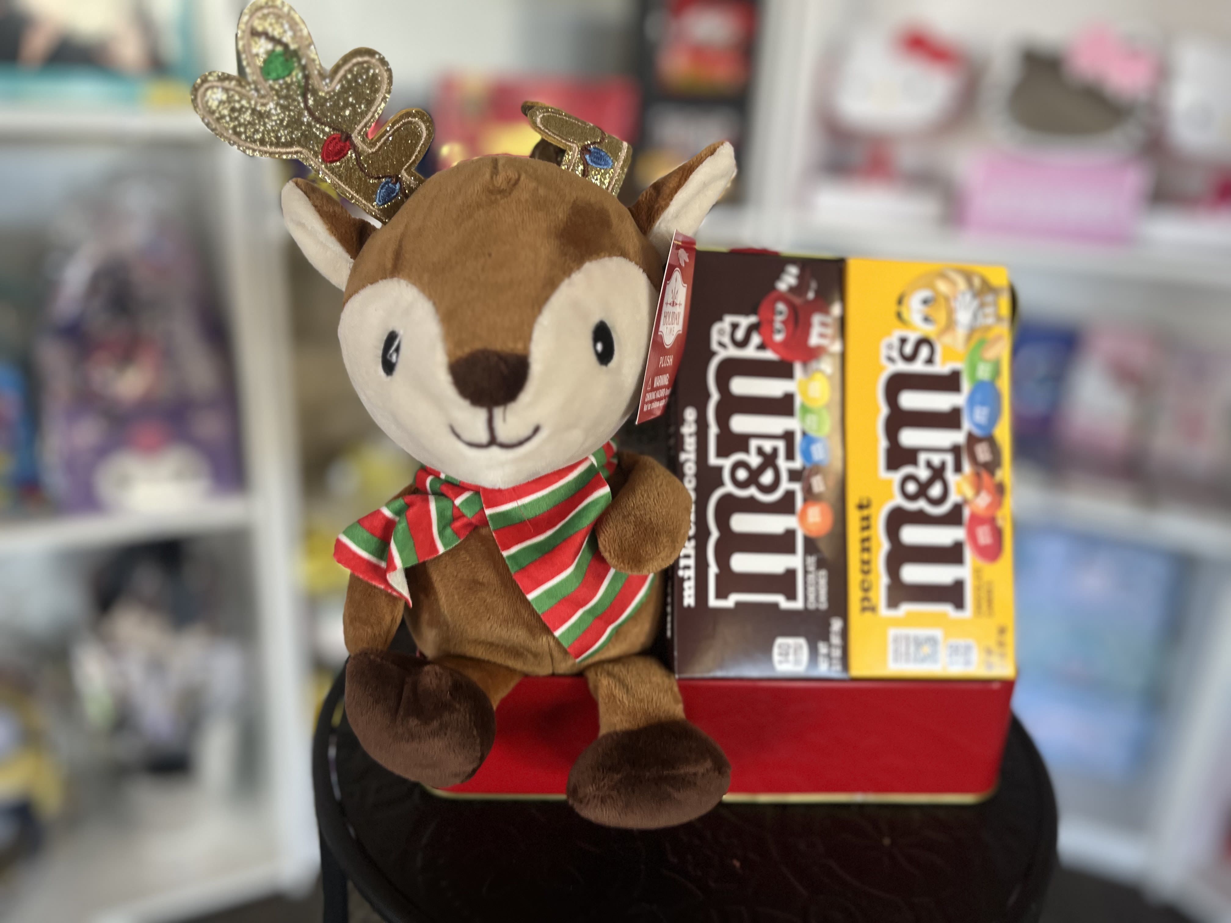 Plush reindeer with a striped scarf beside two M&amp;M's candy boxes