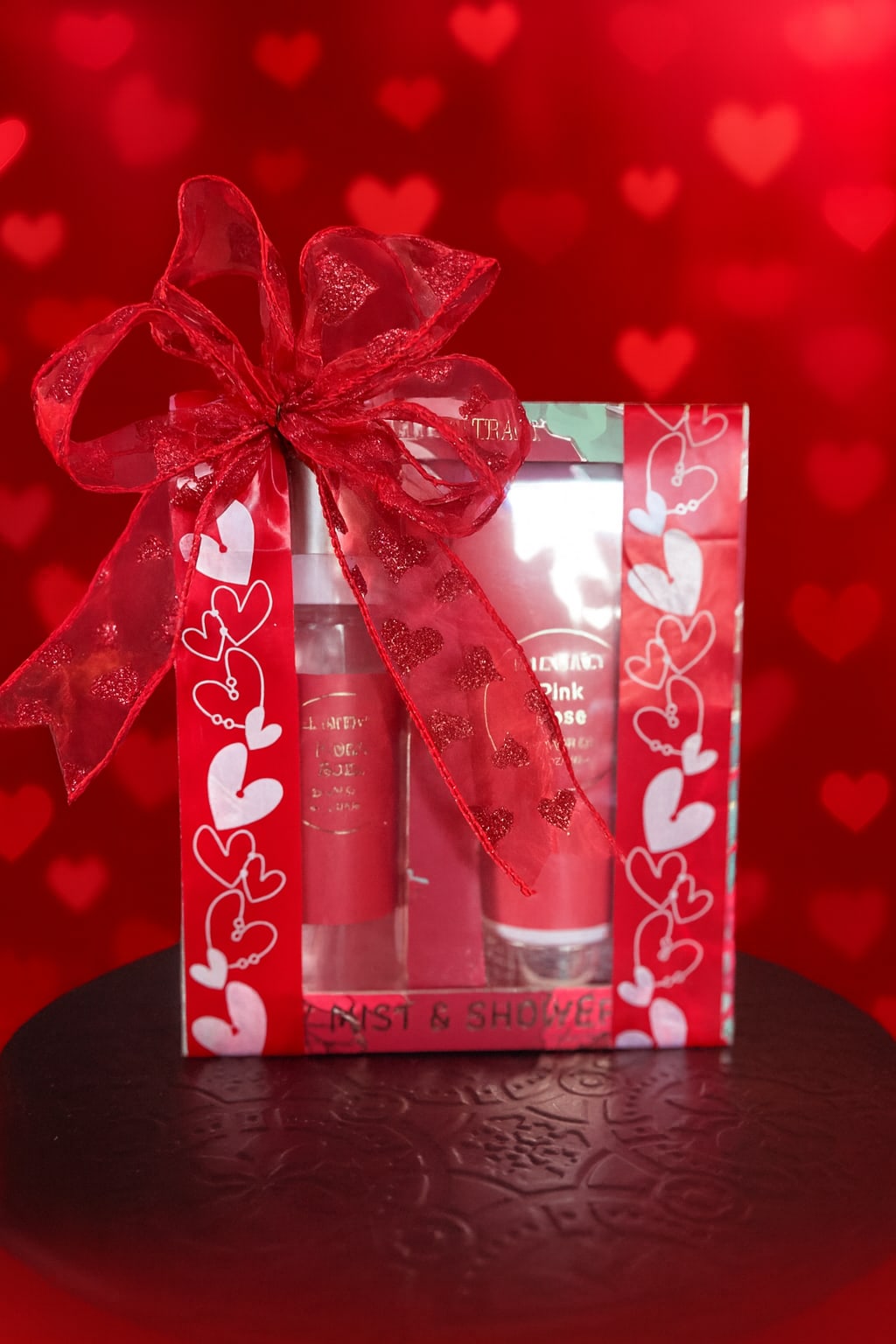 Gift box with red heart ribbon and two pink cosmetic tubes