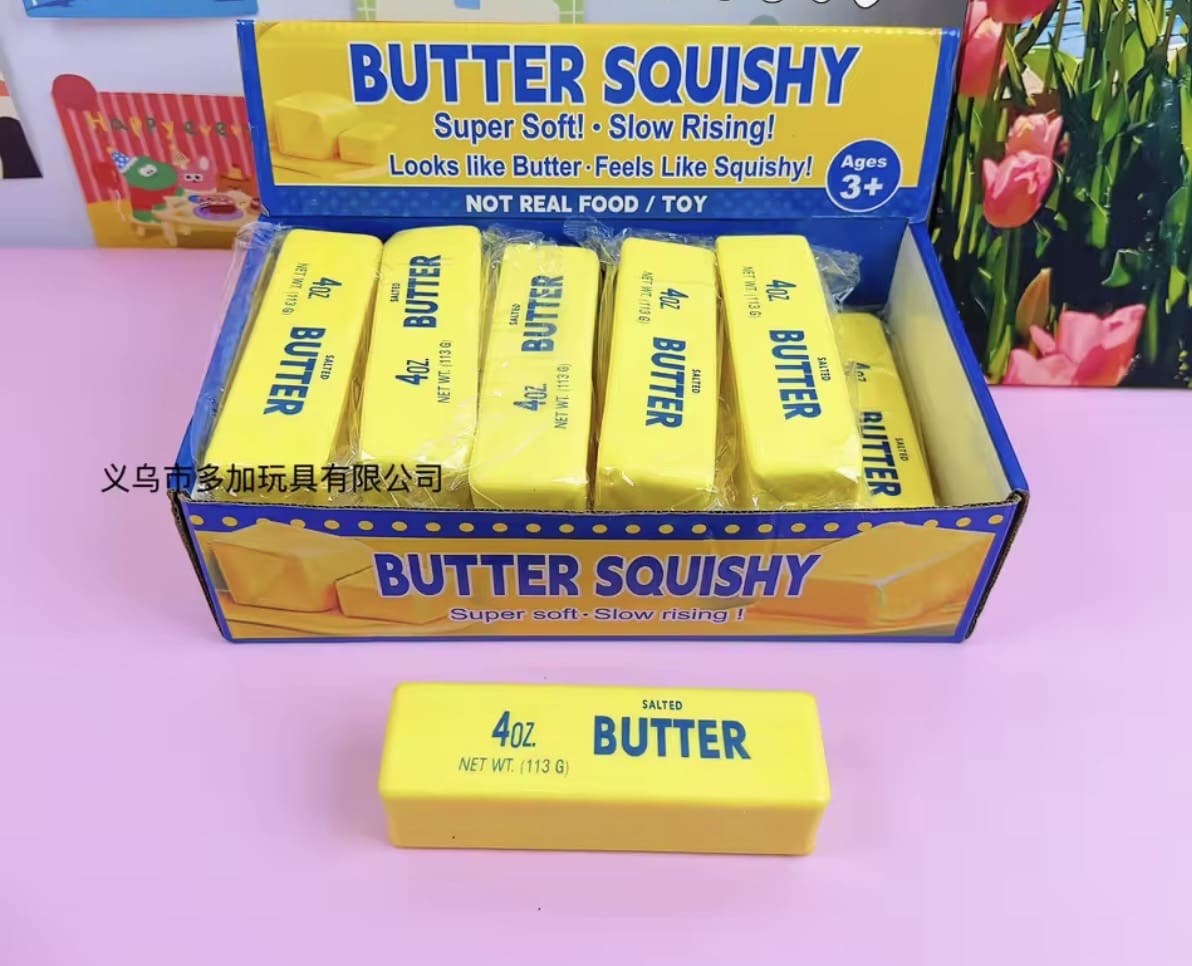 Box of yellow butter-shaped squishy toys on a pink surface