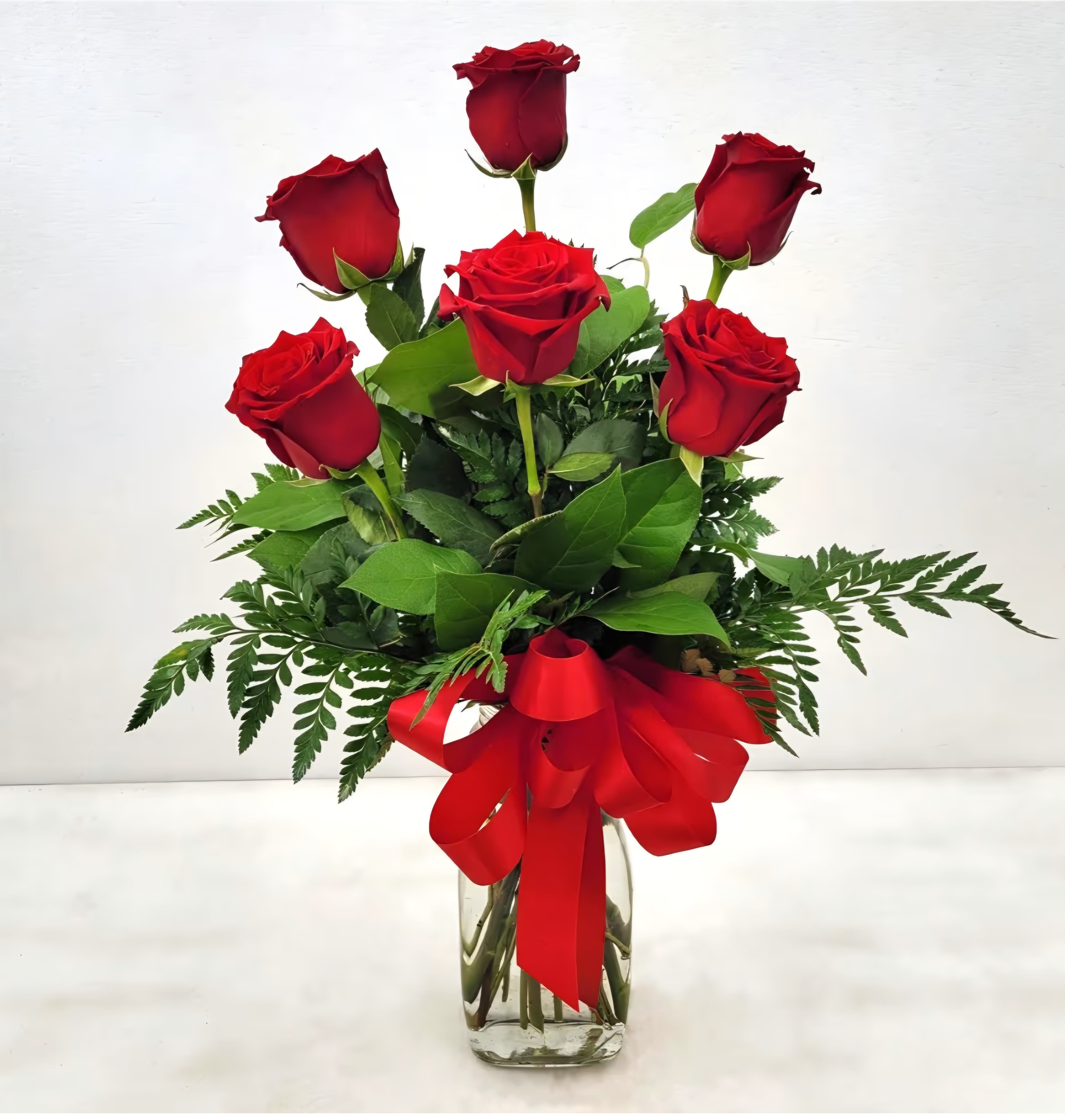 Red roses arranged in a clear glass vase with a red ribbon