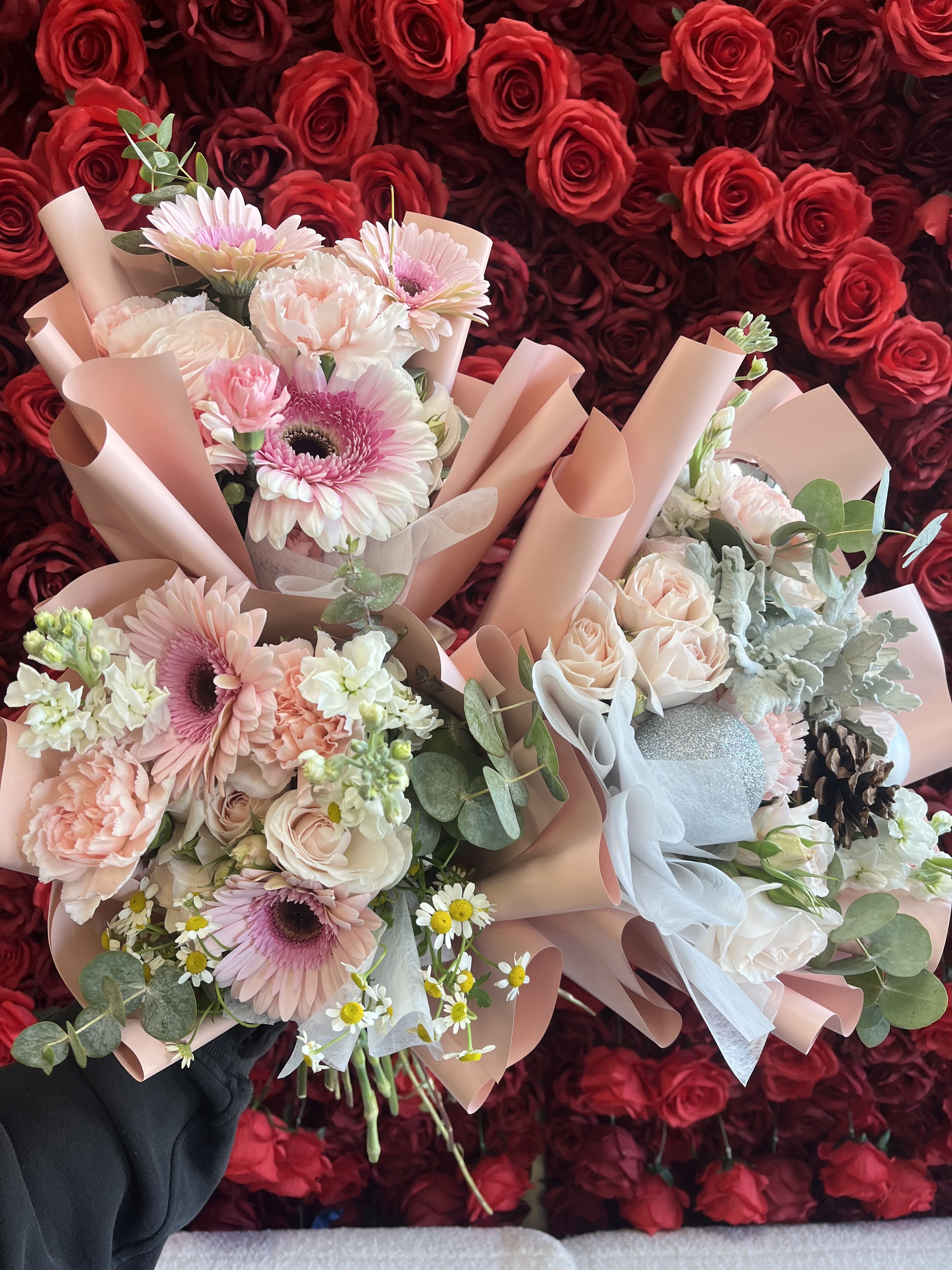 Two pastel bouquets with roses, gerbera daisies, and carnations against a red rose wall