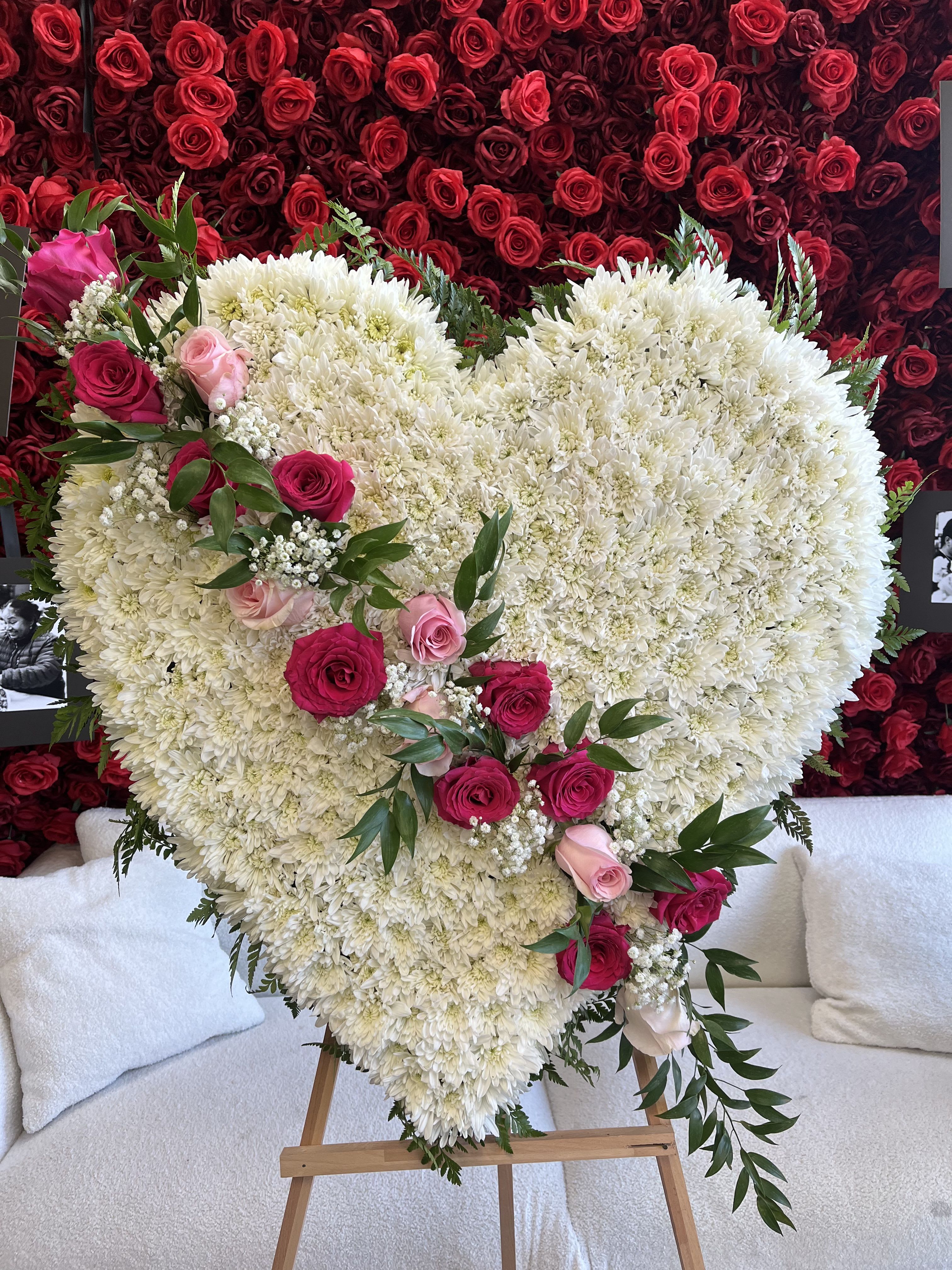 Heart-shaped white floral arrangement with pink roses on an easel