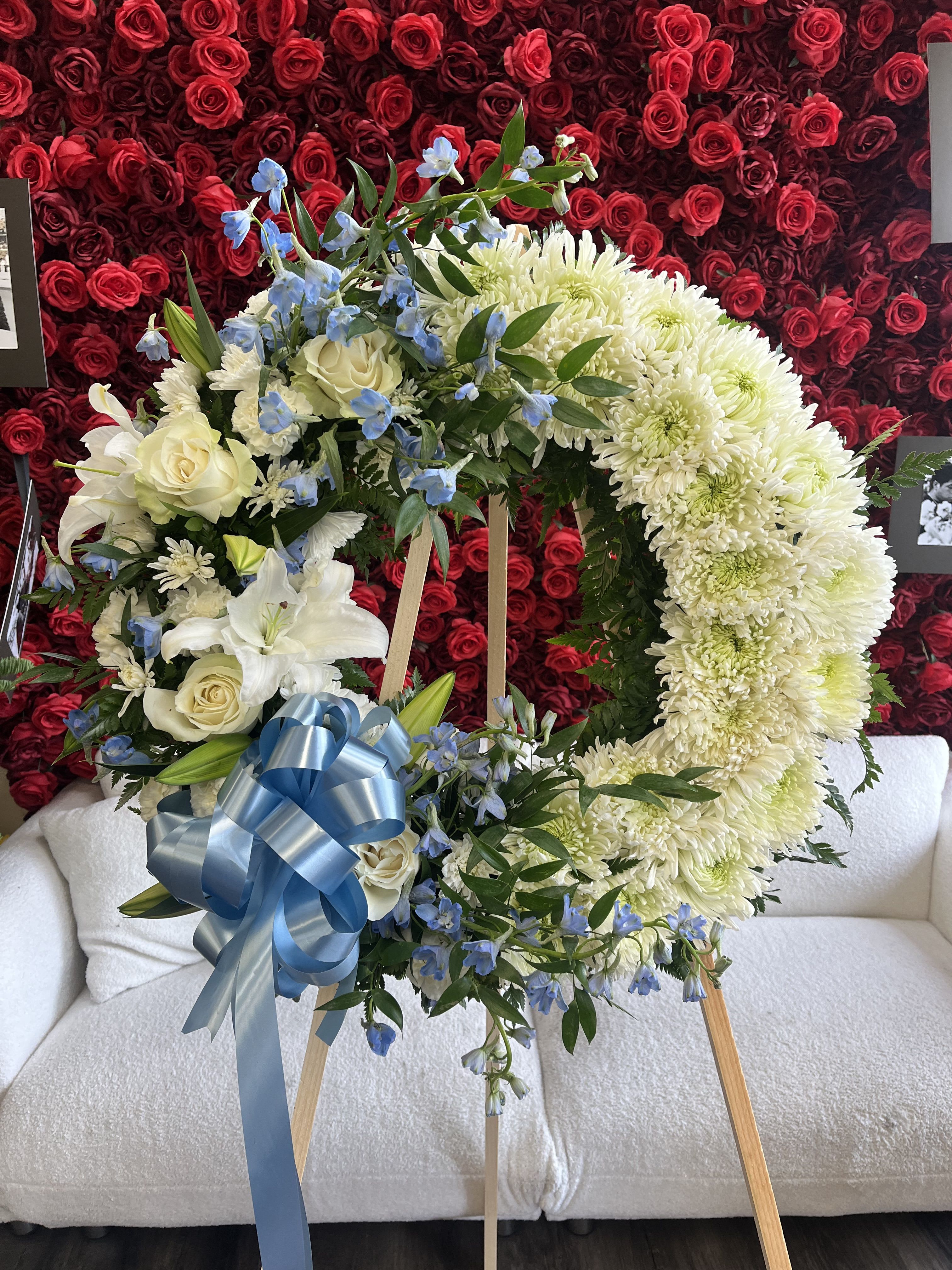 Heart-shaped floral wreath with white flowers, blue accents, and a blue ribbon