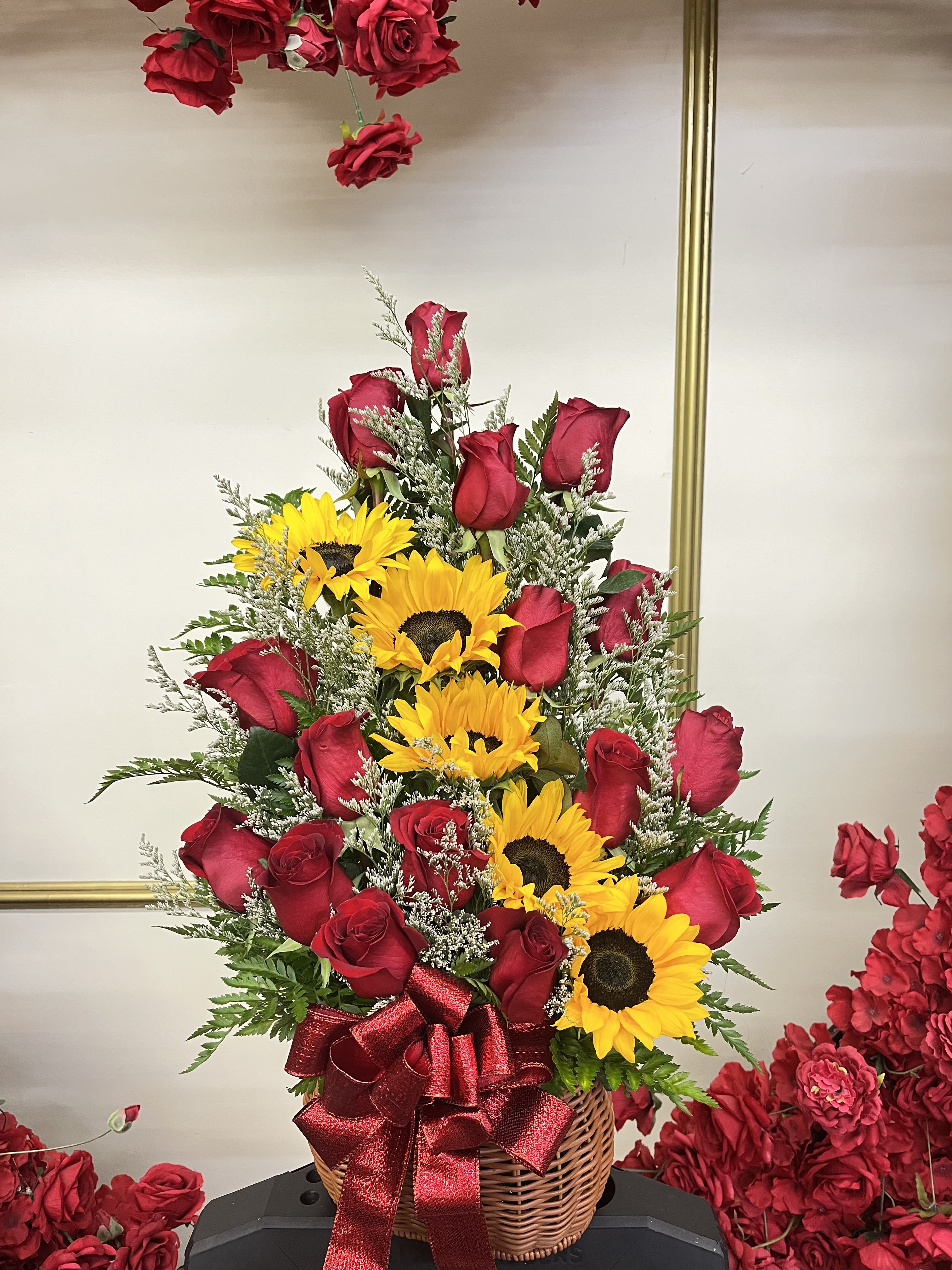 Basket arrangement of red roses and yellow sunflowers with a red ribbon