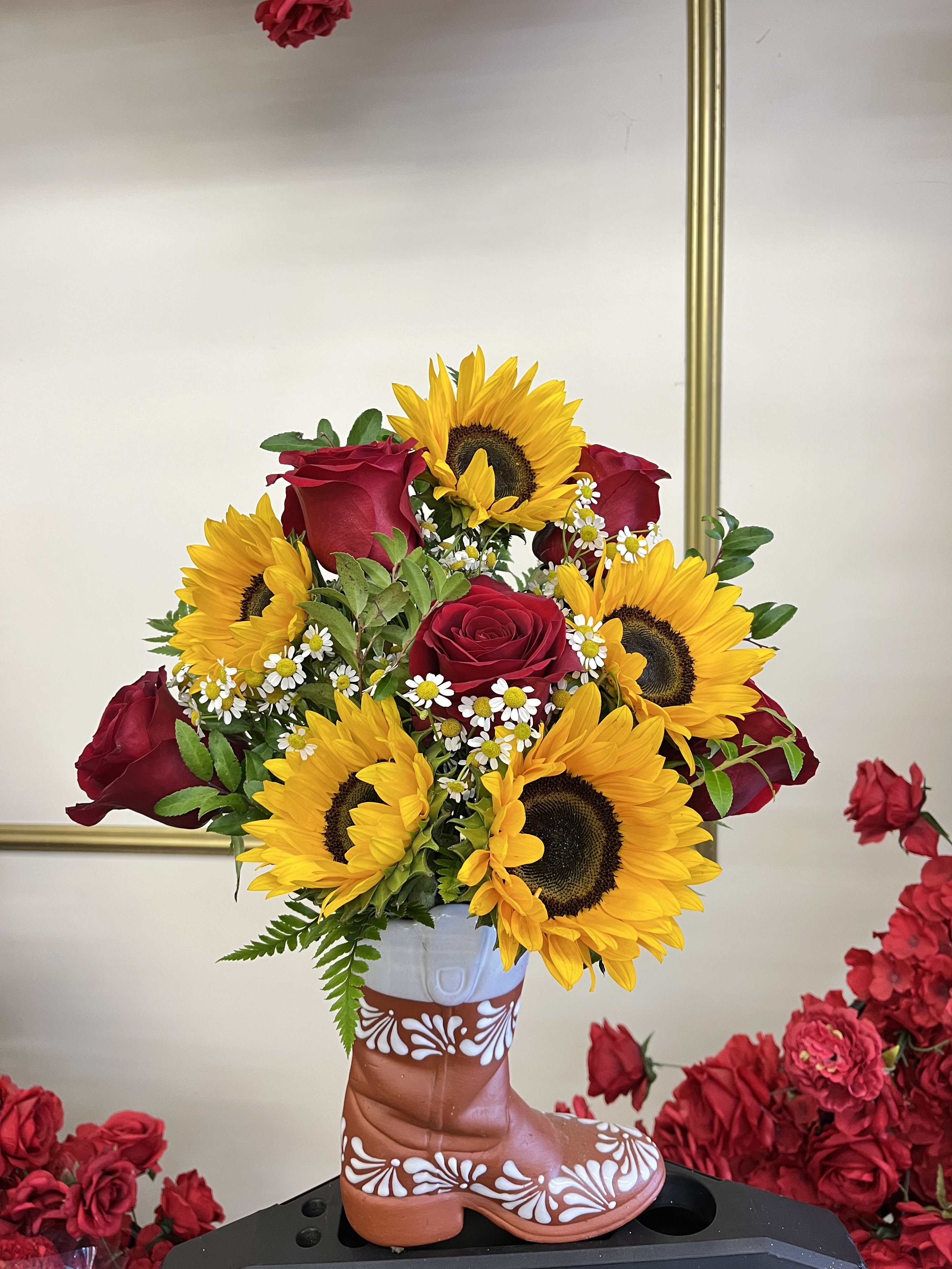 Sunflowers and red roses arranged in a decorative boot vase
