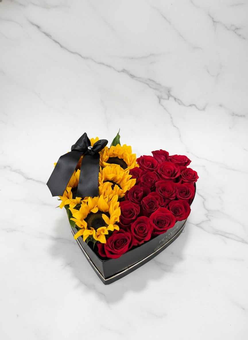 Heart-shaped box with red roses and yellow sunflowers tied with a black ribbon