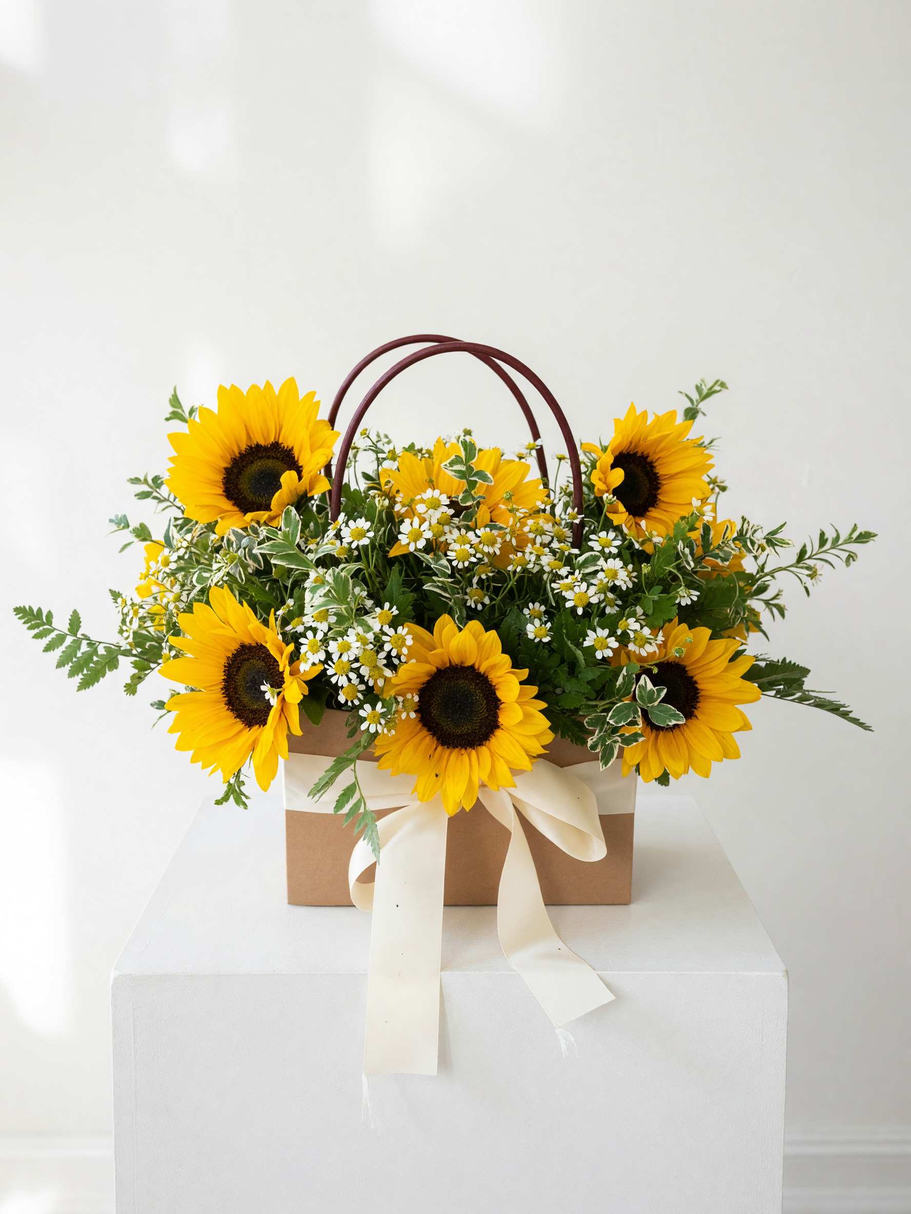 Basket arrangement of sunflowers and small white daisies with a ribbon bow