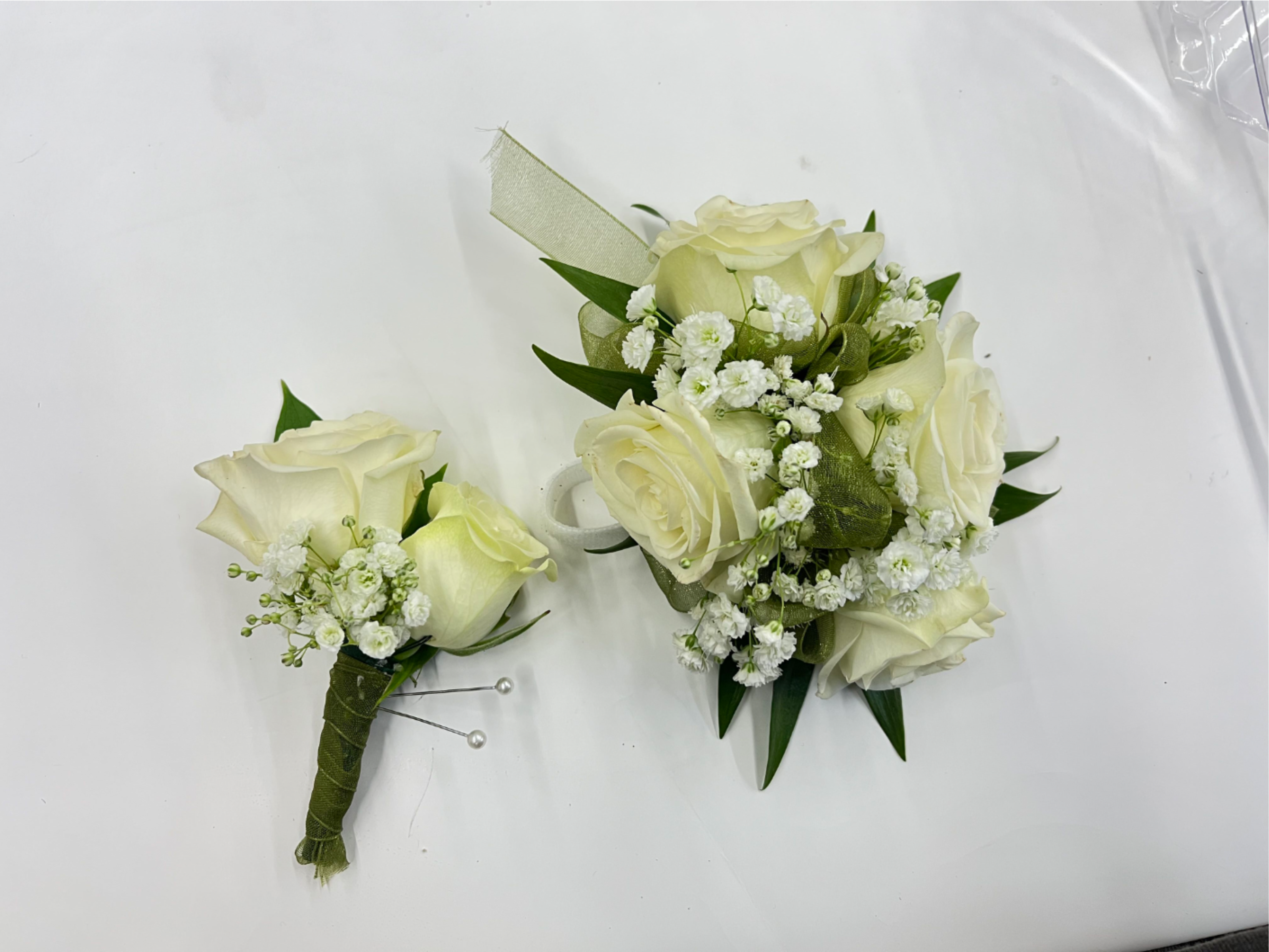 White Rose Corsage &amp; Boutonnière  - White rose corsage and boutonniere set accented with baby’s breath for a soft, classic look. The corsage comes on an adjustable Velcro wristlet, and the boutonniere is attached with a magnet for easy wear. Ribbon color is customizable, please add your choice in the special instructions.