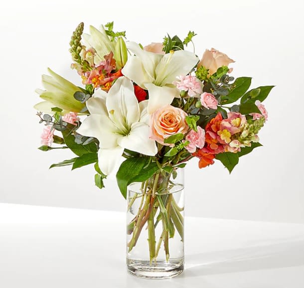 Bouquet of white lilies and peach roses in a clear glass vase