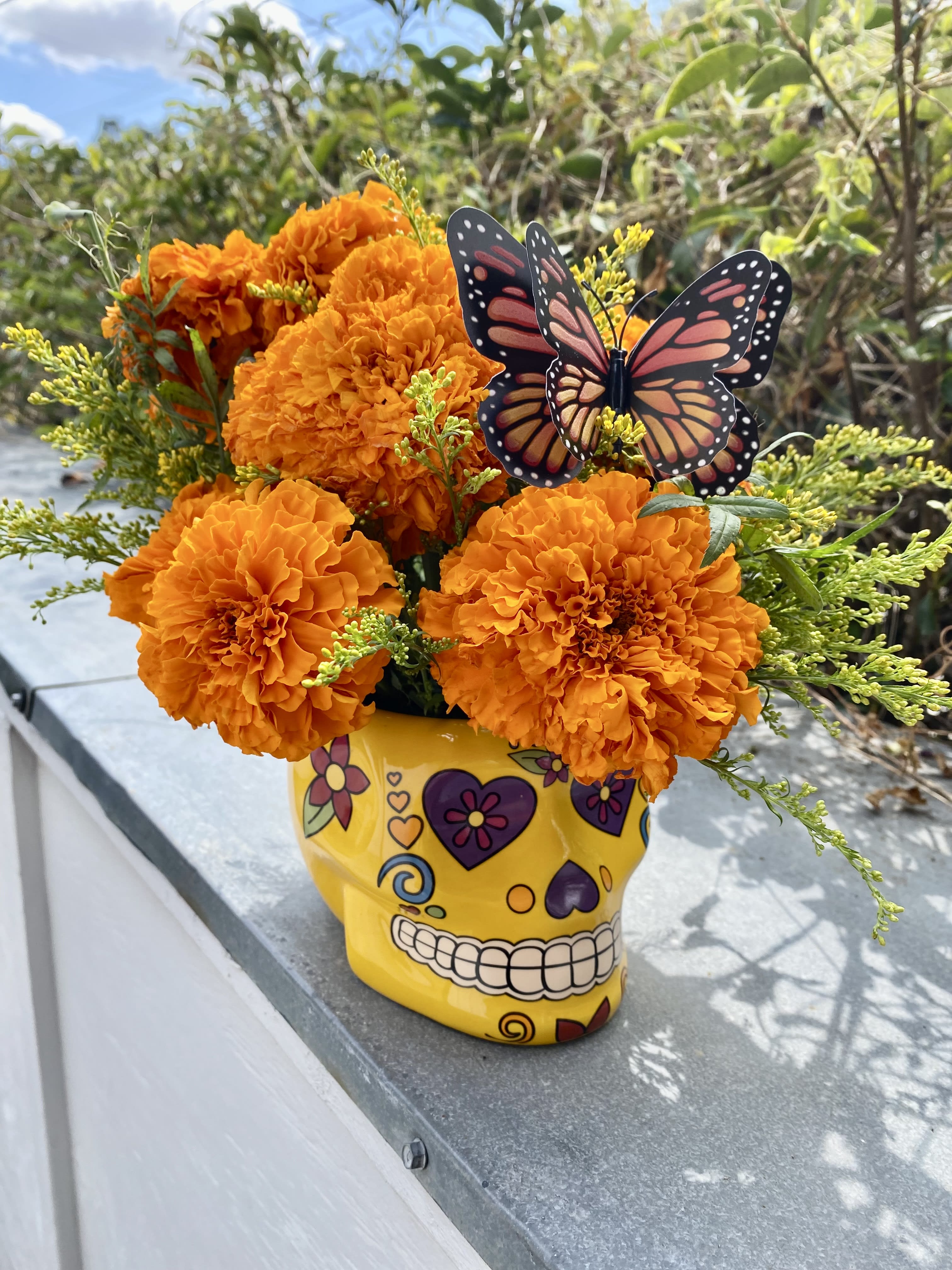 Orange marigold bouquet in a yellow skull vase with a butterfly pick