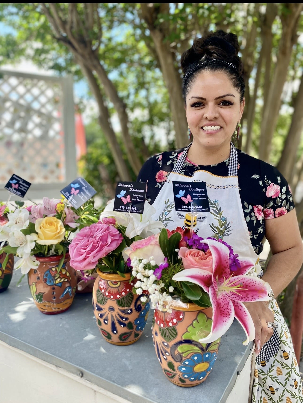 Woman holding colorful flower arrangements in painted ceramic vases outdoors.