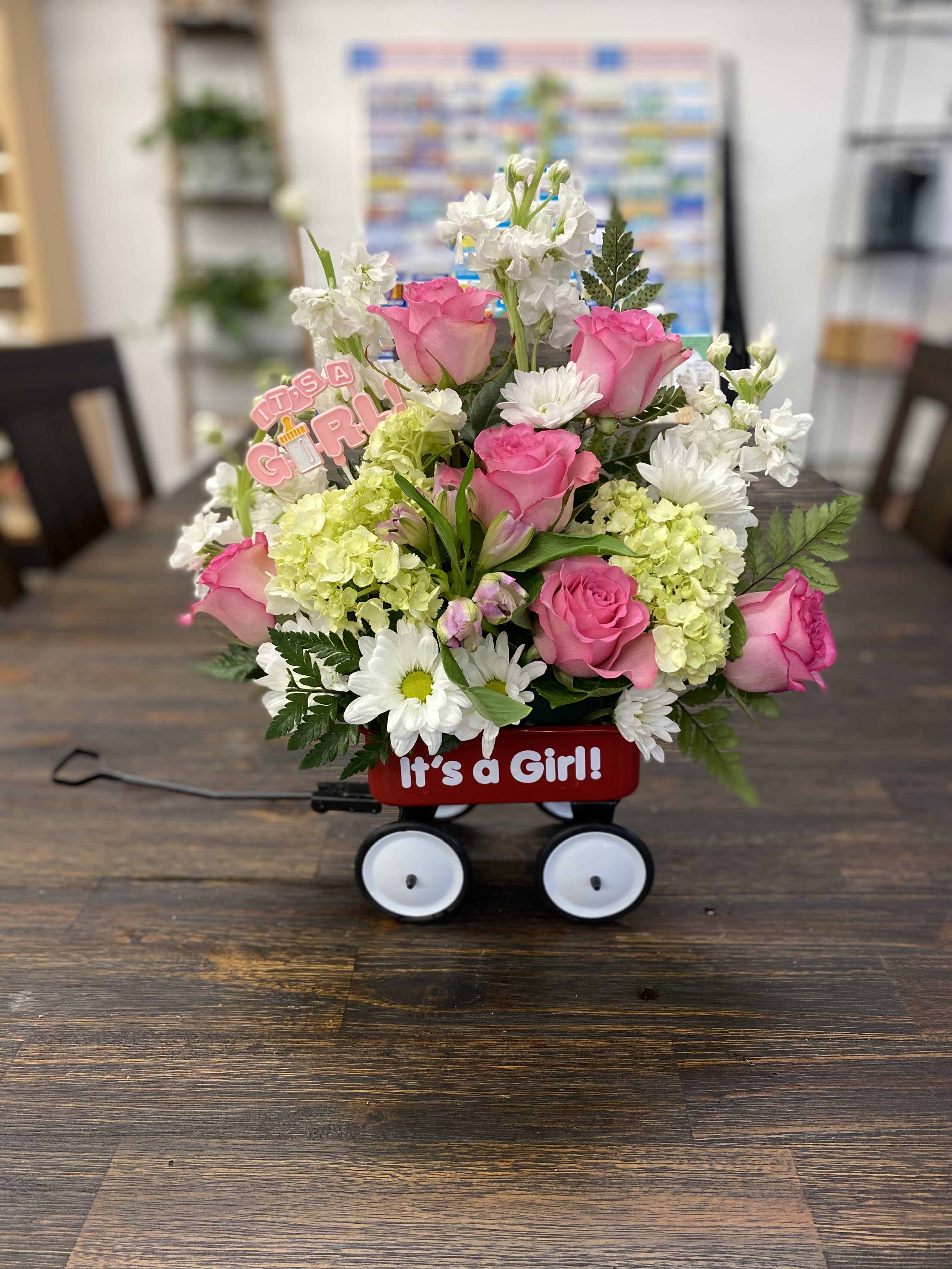 Pink roses and white flowers in a red wagon with an "It's a Girl!" sign