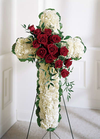 Cross-shaped floral tribute with red roses and white flowers on a stand
