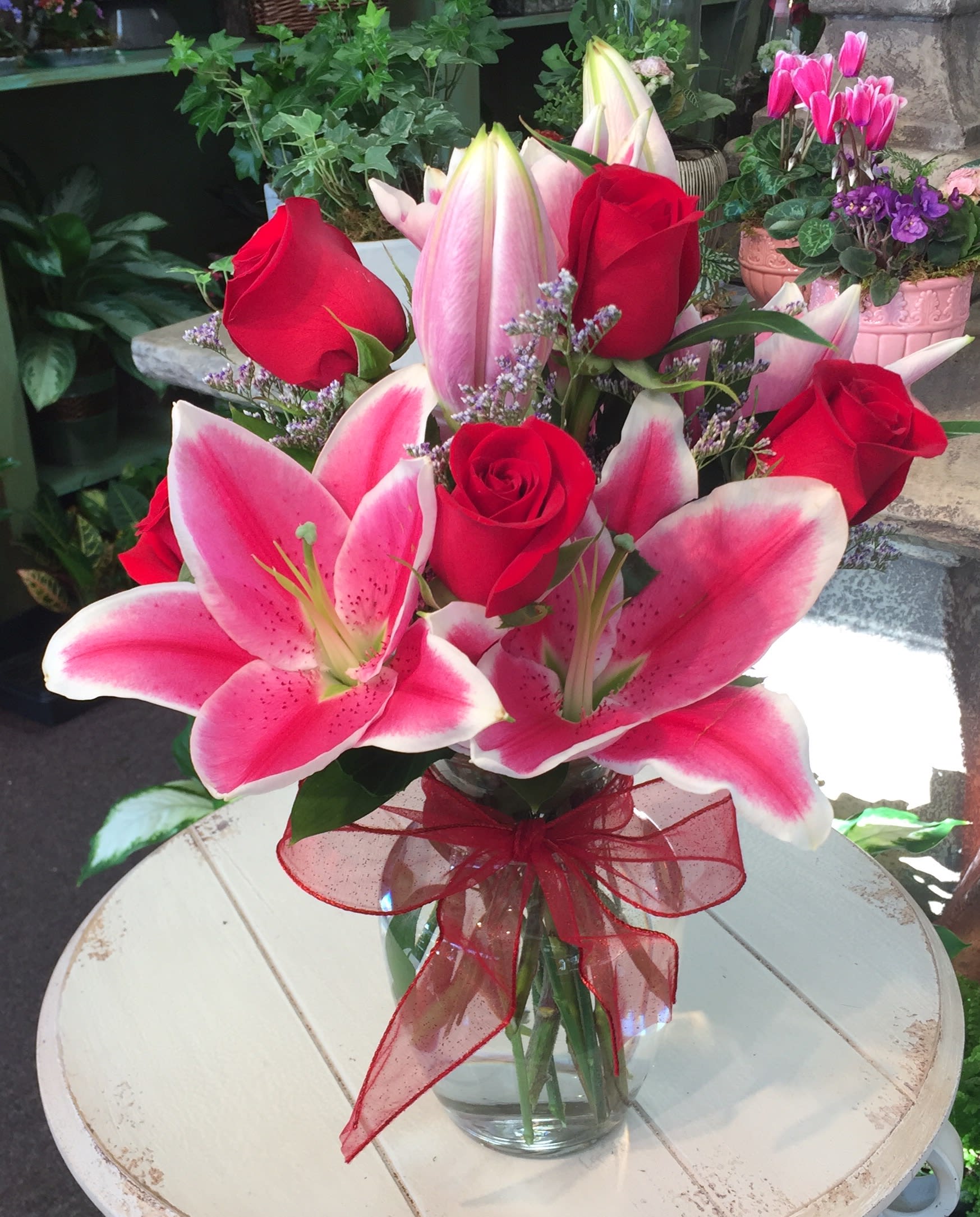 Bouquet of pink lilies and red roses in a glass vase with a red ribbon