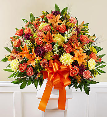 Large bouquet of orange and pink flowers with a ribbon in a white vase