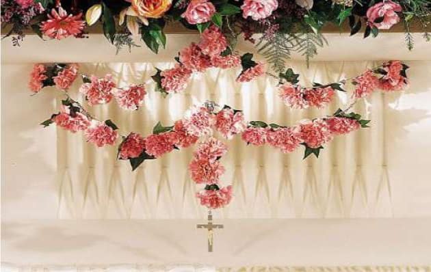 Pink floral garlands draped over a white draped backdrop with a hanging cross