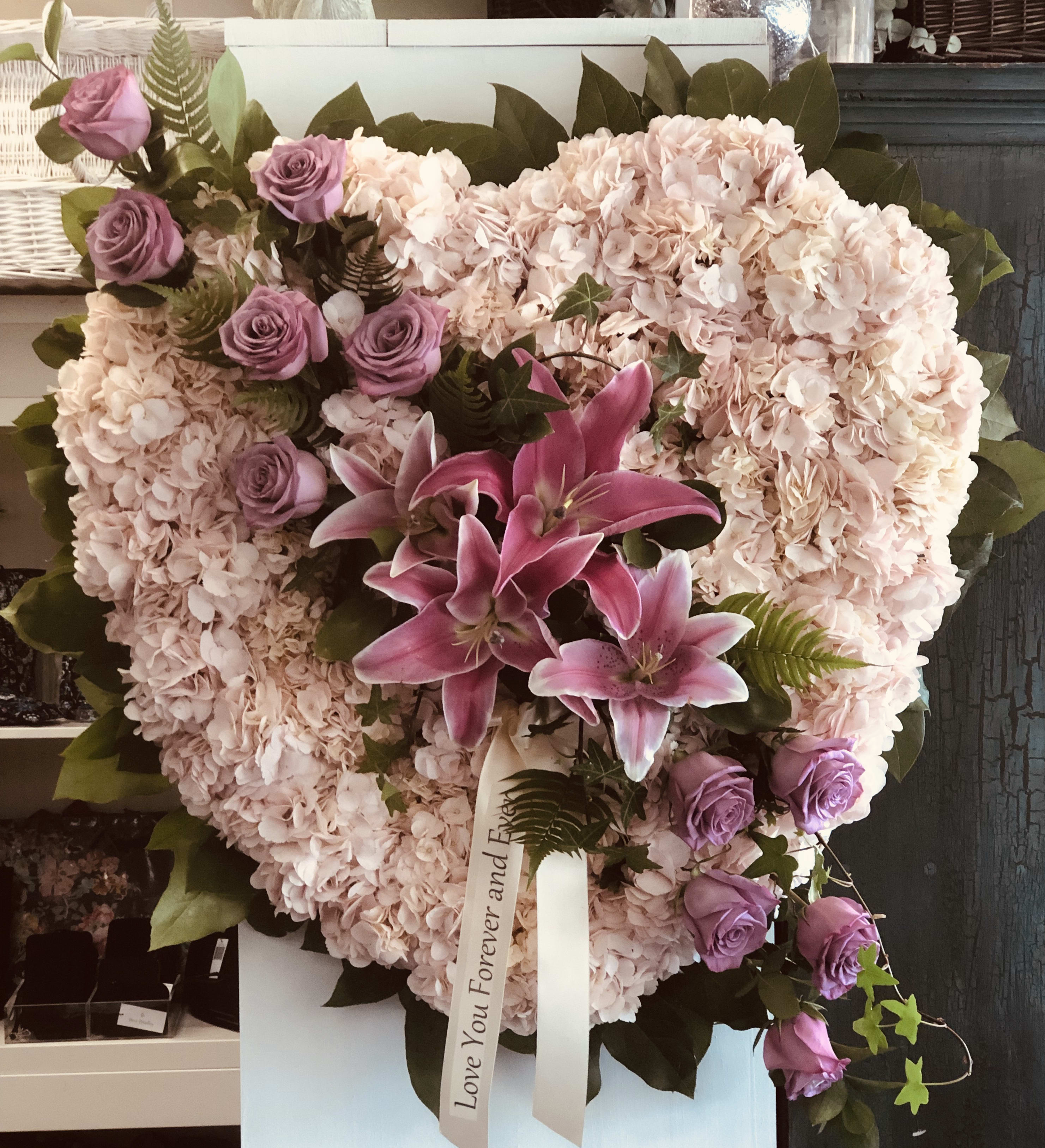 Heart-shaped floral arrangement with pink hydrangeas, purple roses, and lilies