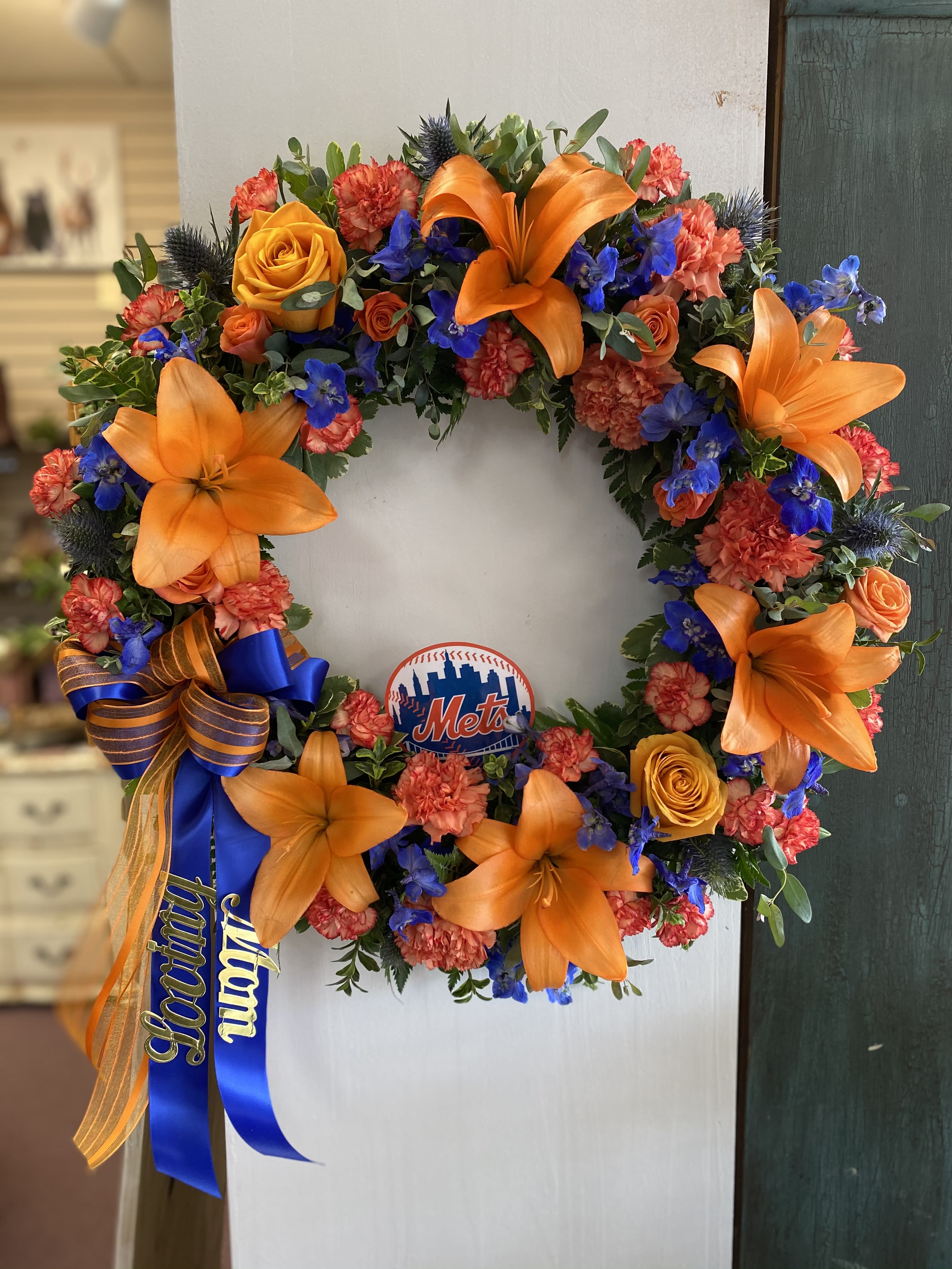 Circular floral wreath with orange lilies, roses, and blue flowers