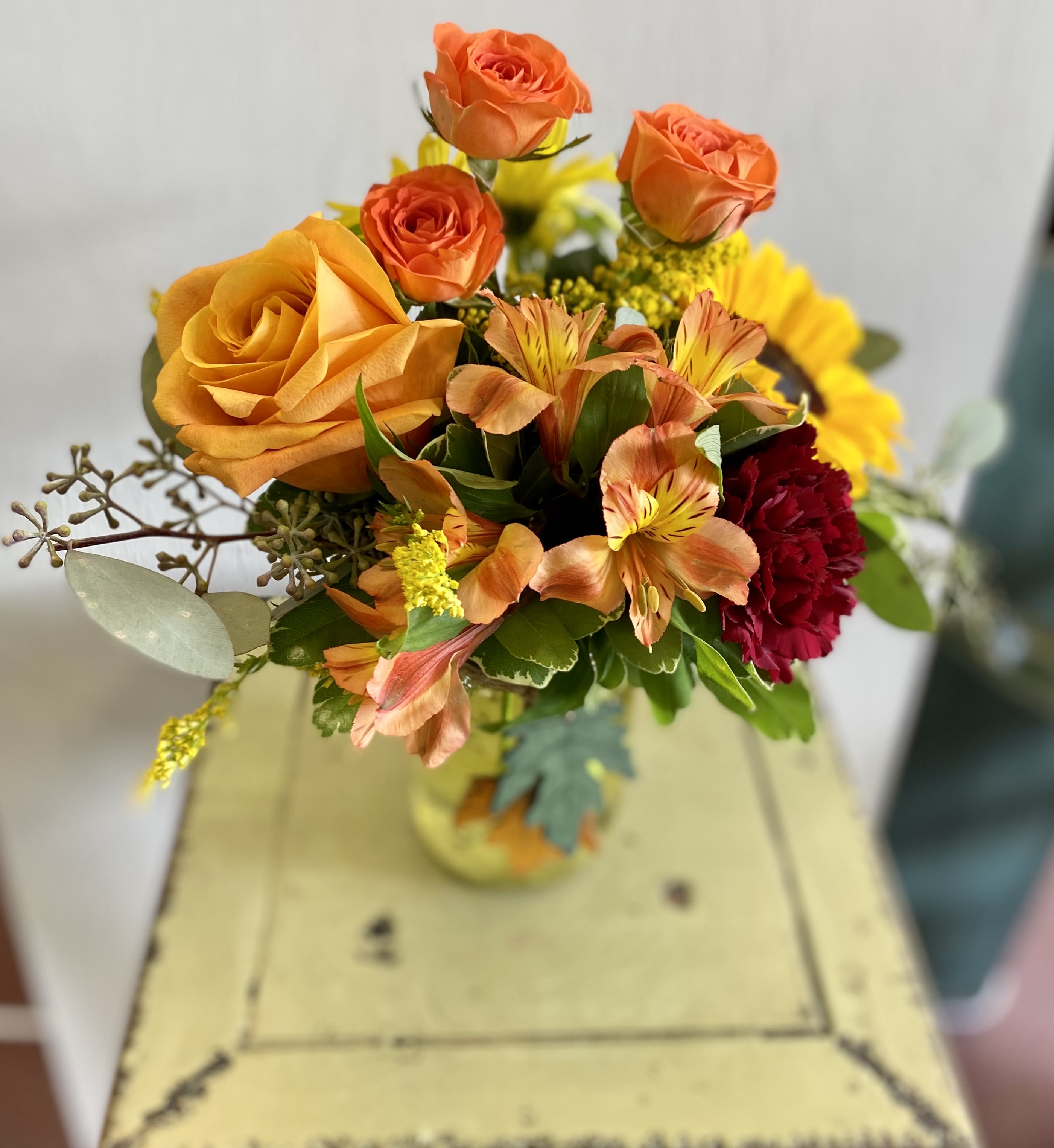 Bouquet of orange and yellow roses with mixed flowers in a glass vase