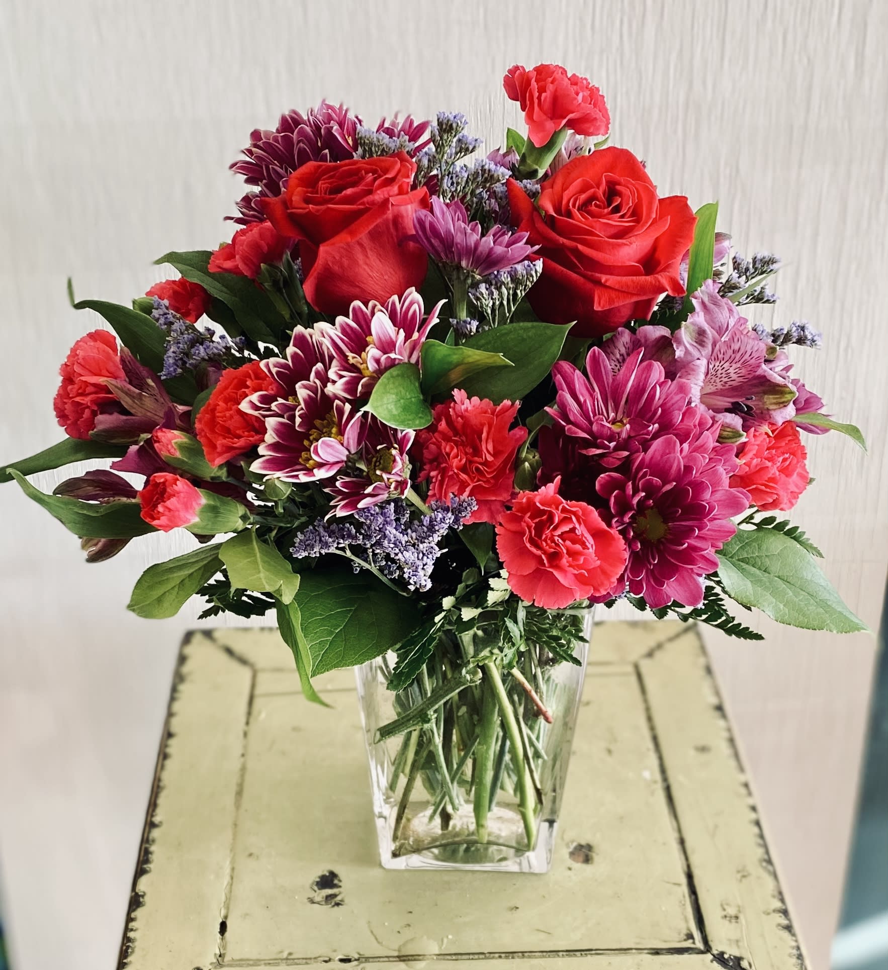 Bouquet of red roses, pink carnations, and purple chrysanthemums in a clear vase