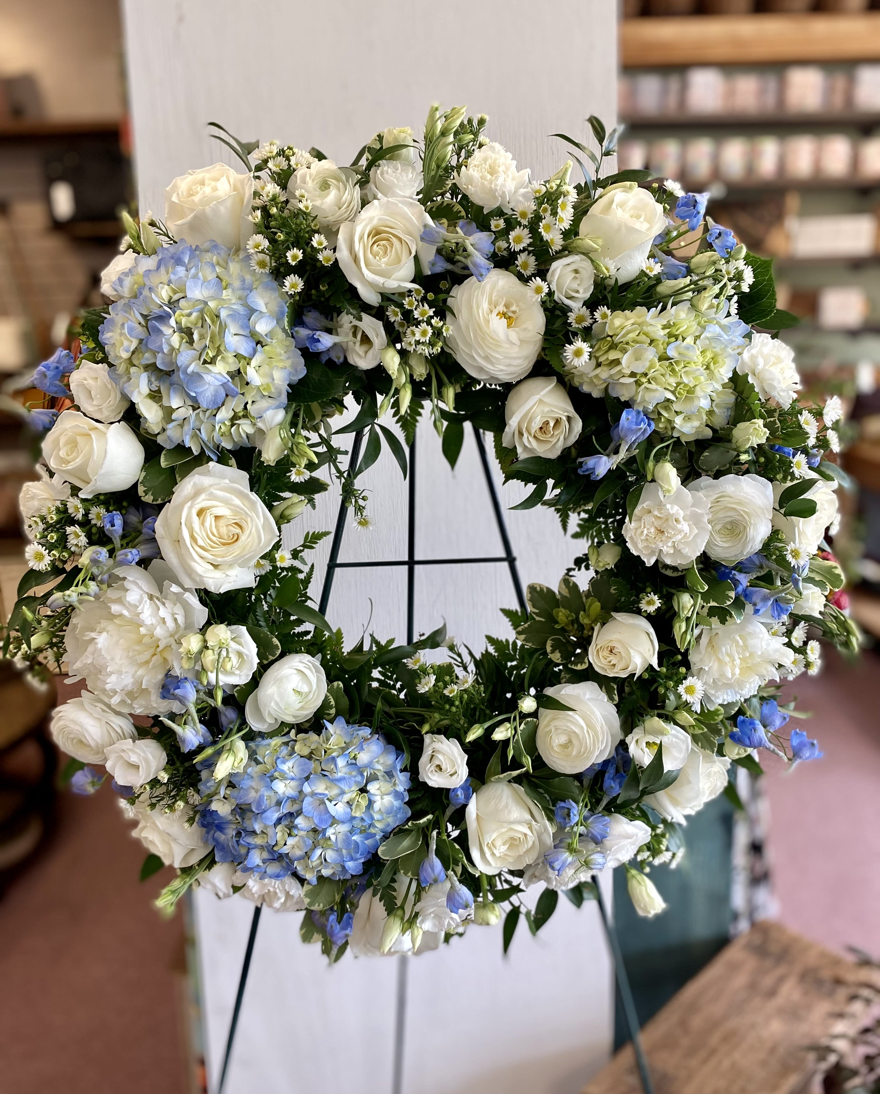 Large white floral wreath with blue accents on a stand