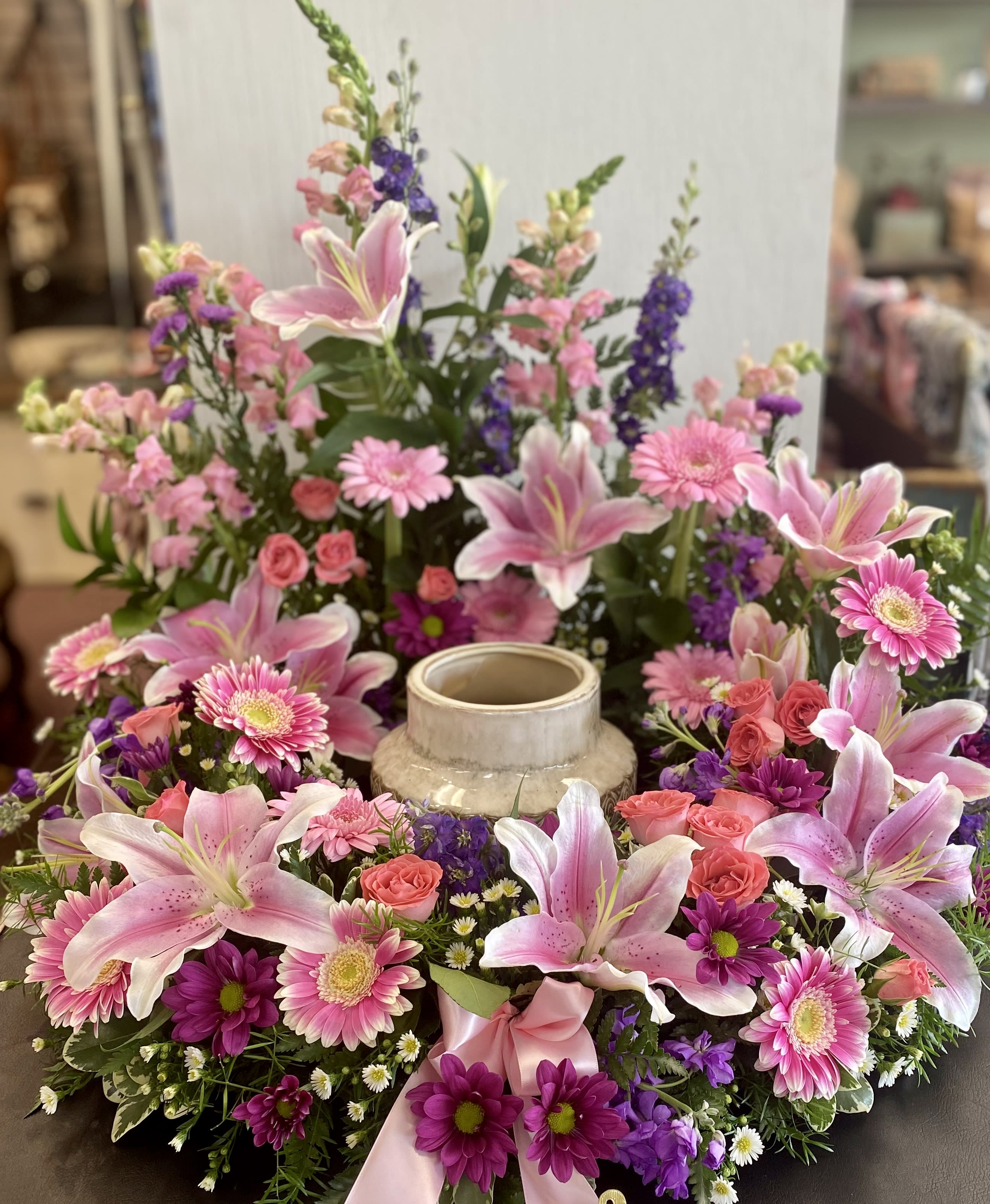 Peaceful Memories Wreath - A lovely wreath to encircle an urn.  Pink lilies accented with roses and lovely blooms in lavender and pink hues along with lush greens create a lovely arrangement piece that brings peace and solace. Standard = 18" form, approx 24" finished width Deluxe  = 24" form, approx 30" finished width 