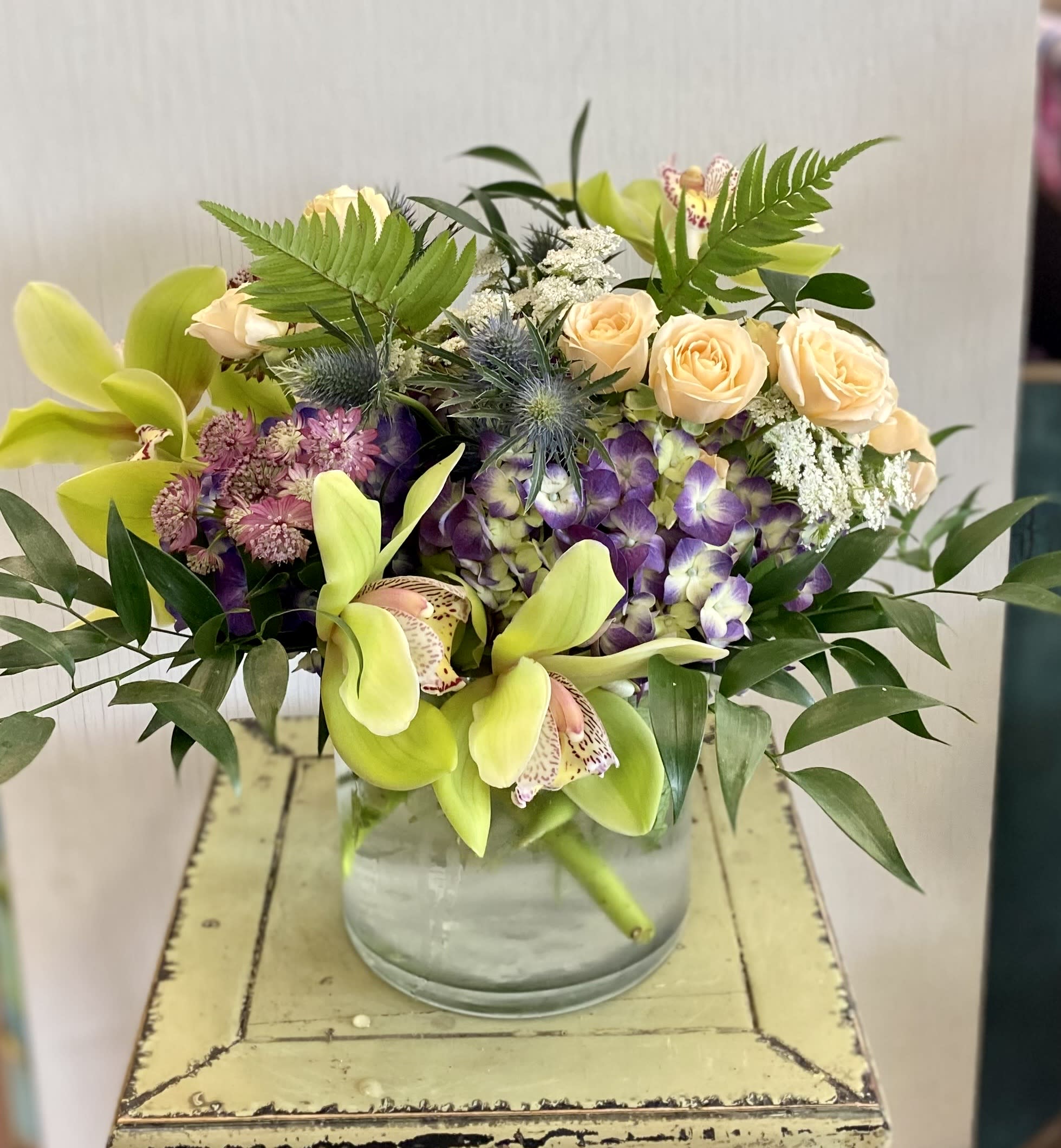 Mixed bouquet in a glass vase with orchids, roses, and purple blooms