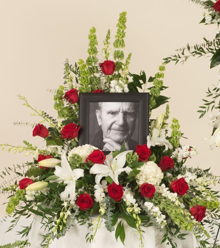 Sympathy floral display with red roses, white lilies, and a framed portrait