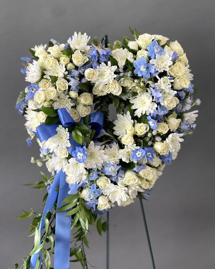 Heart-shaped wreath of white and blue flowers with a blue ribbon