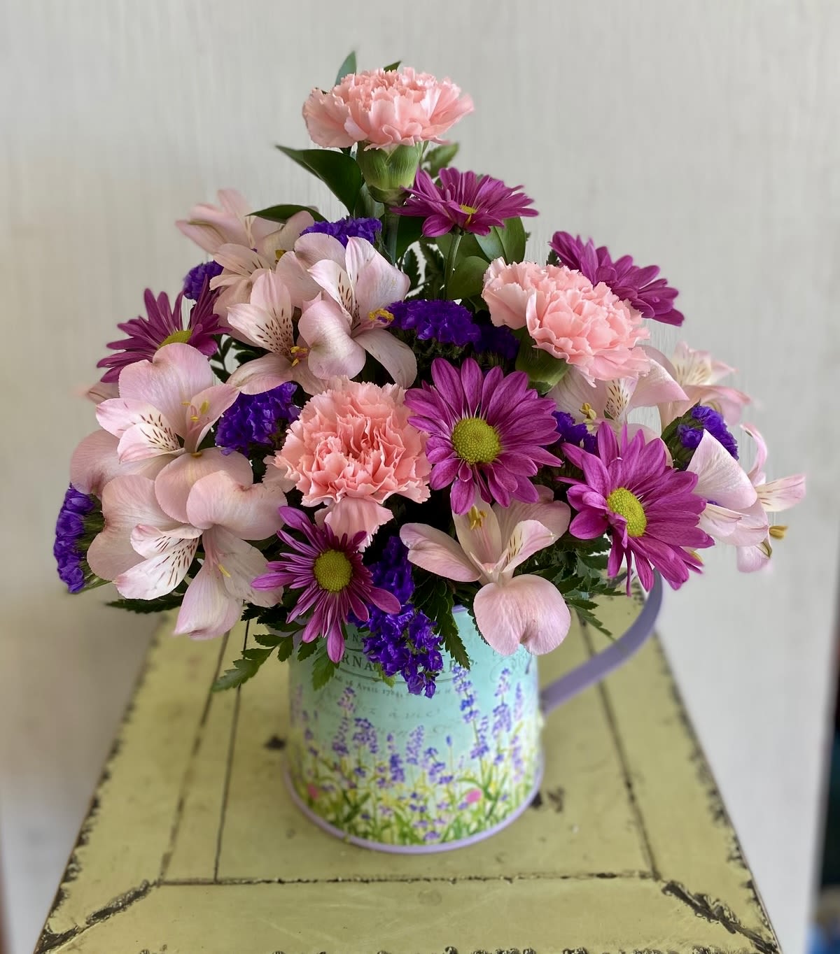 Pink and purple mixed flowers arranged in a decorative metal container