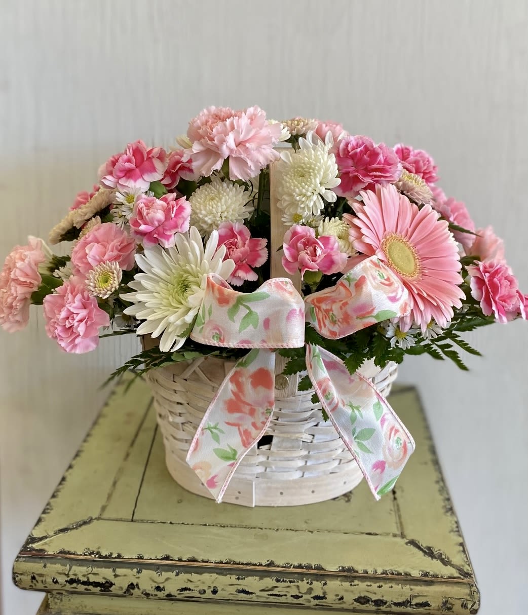 Pink and white flowers in a white wicker basket with a floral ribbon
