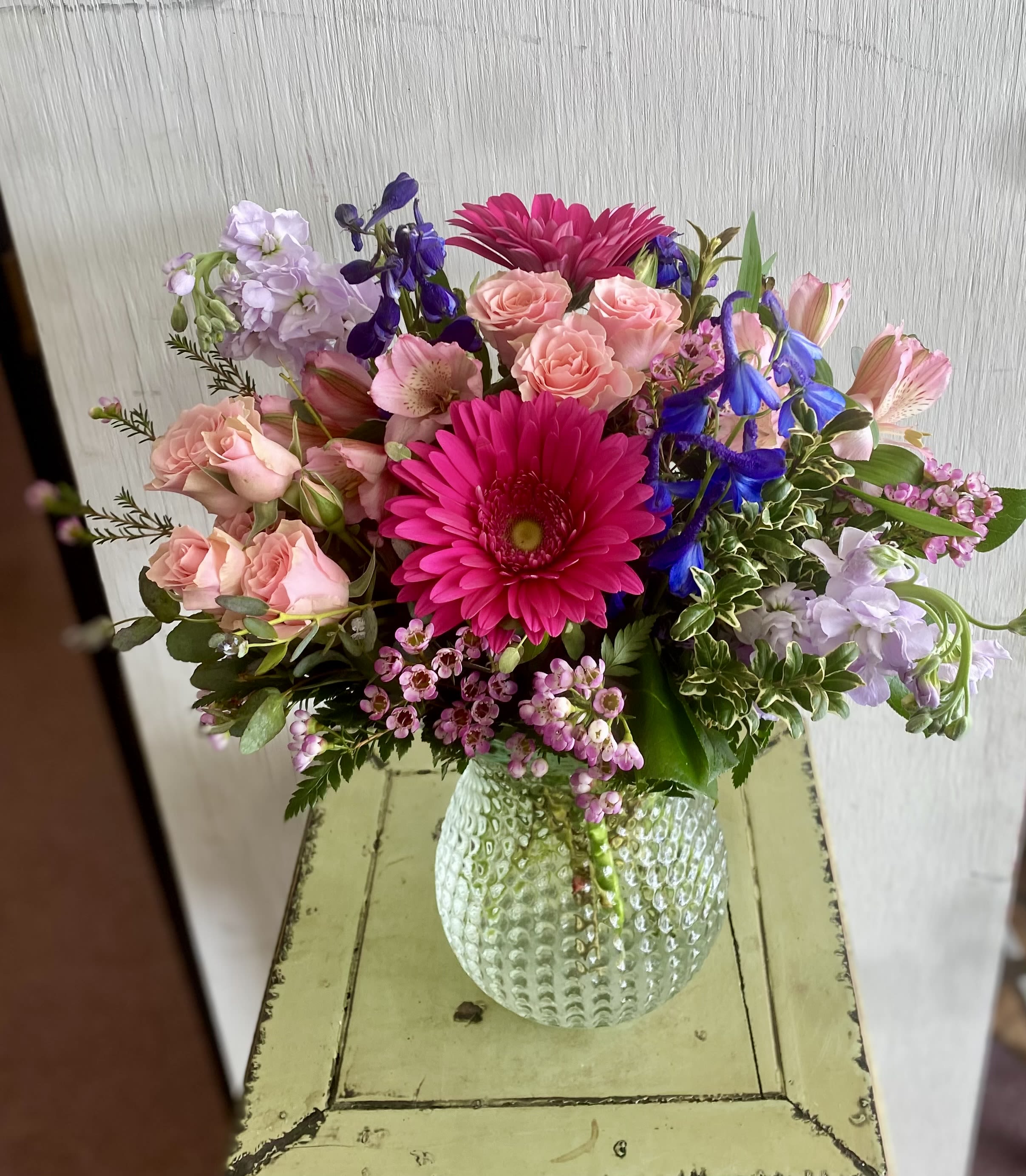 Mixed bouquet of pink, purple, and blue flowers in a textured glass vase