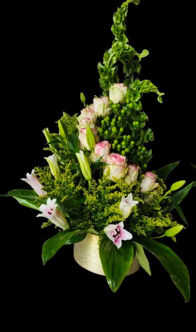 Golden Tower - Pale pink roses and white lilies rise above tall green snapdragon-like spikes in a vertical composition that feels both celebratory and refined-perfect as an anniversary roses arrangement or an elegant birthday bouquet. The Golden Tower flower arrangement makes the recipient feel seen and celebrated: the soft rose petals and fragrant lilies read as heartfelt and intimate, while the upright silhouette brings a stately, joyful presence to any room.  This flower arrangement features pale pink roses, white lilies, and tall green snapdragon-style blooms accented by bright yellow filler flowers and glossy green foliage. The layered, upright design is arranged densely at the base for texture and contrast, then tapers upward for a graceful profile. Everything is presented in a round, light-colored ceramic vase that gives the display a polished, gift-ready finish.  Ideal for marking anniversaries, milestone birthdays, or sending congratulations, this arrangement suits someone who appreciates classic blooms with a modern vertical twist. Care is simple: keep water fresh, trim stems every few days, and display away from direct heat to prolong the life of the roses and lilies.