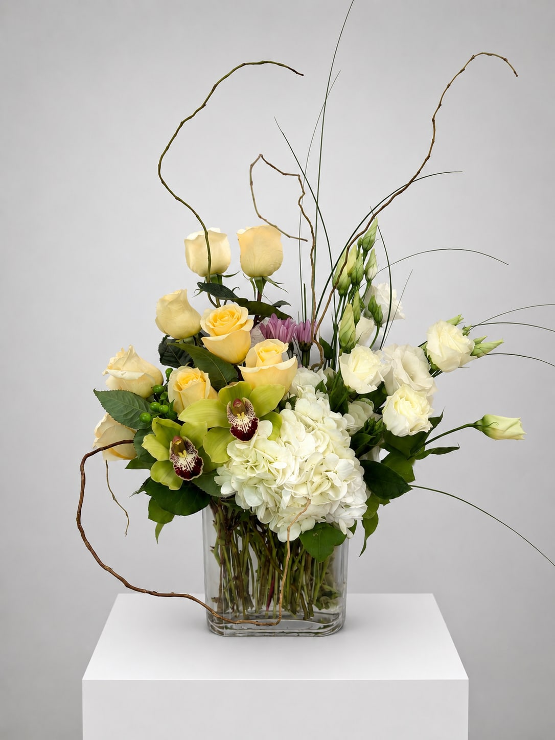 Mixed bouquet of yellow roses, white hydrangea, and orchids in a glass vase