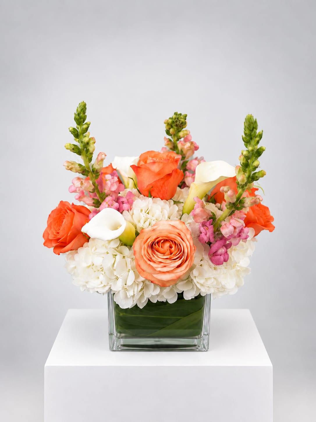 Orange and white floral arrangement in a square glass vase