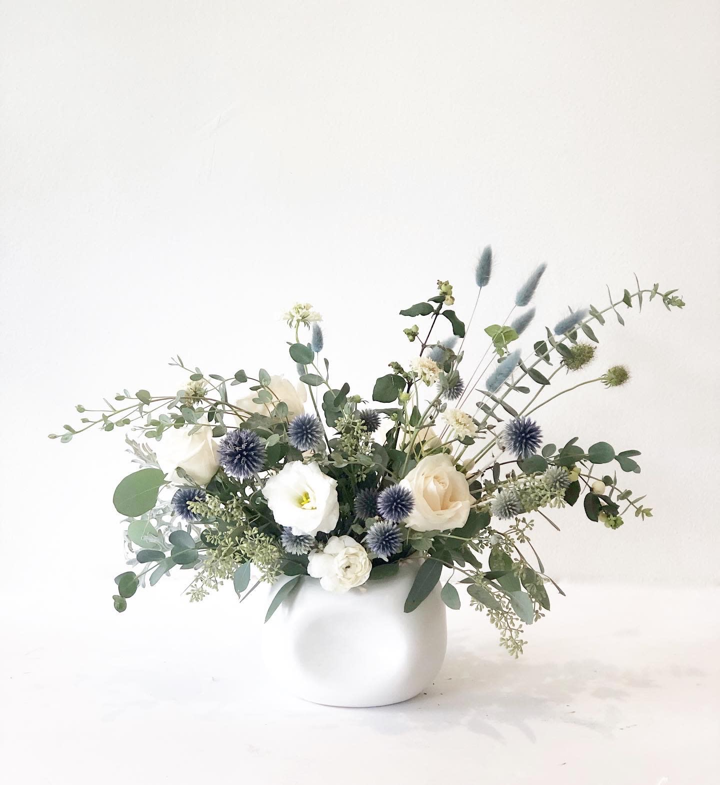 White and cream flowers in a round white vase with blue thistle-like blooms