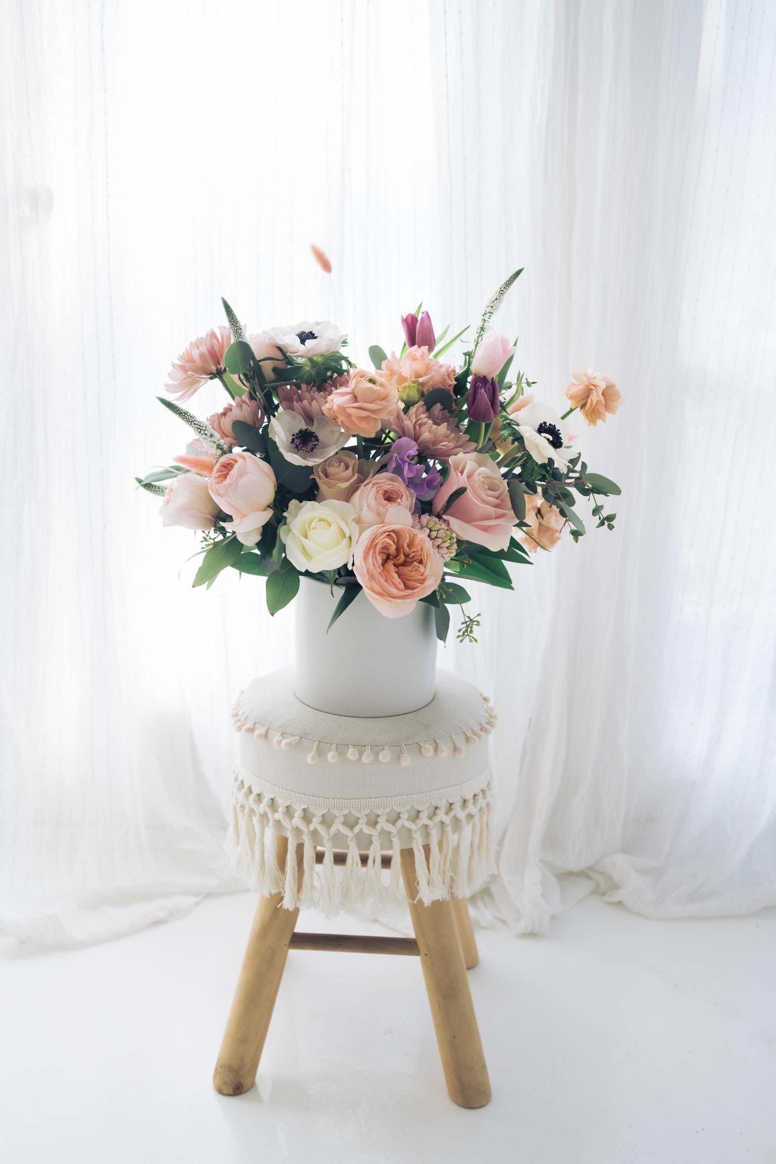 Pastel flower arrangement in a white vase on a stool