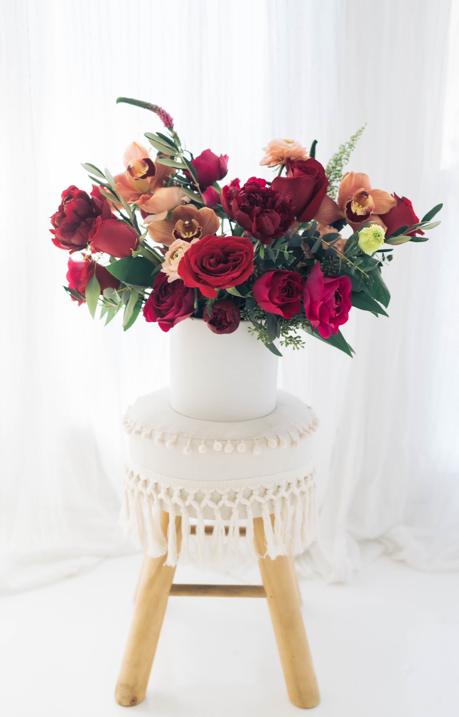 Red and peach floral arrangement in a white vase on a stool