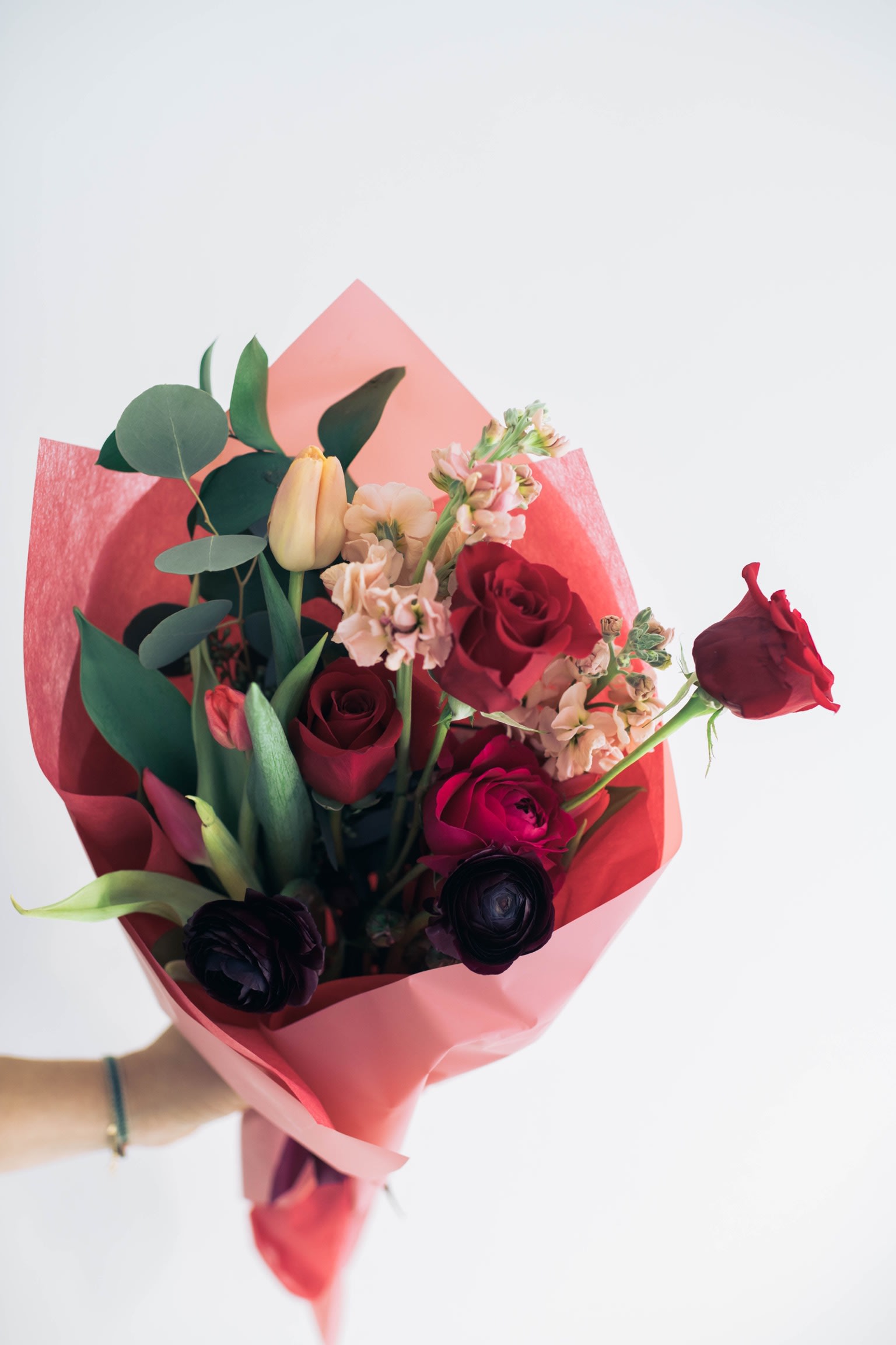 Bouquet of red roses, tulips, and pale pink flowers wrapped in pink paper
