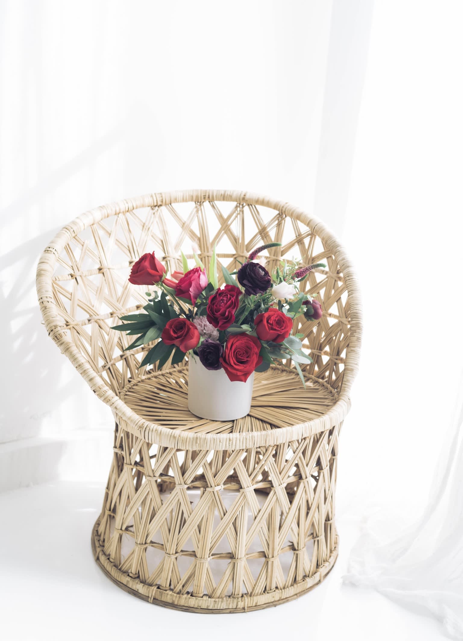 Red rose arrangement in a white vase on a wicker chair