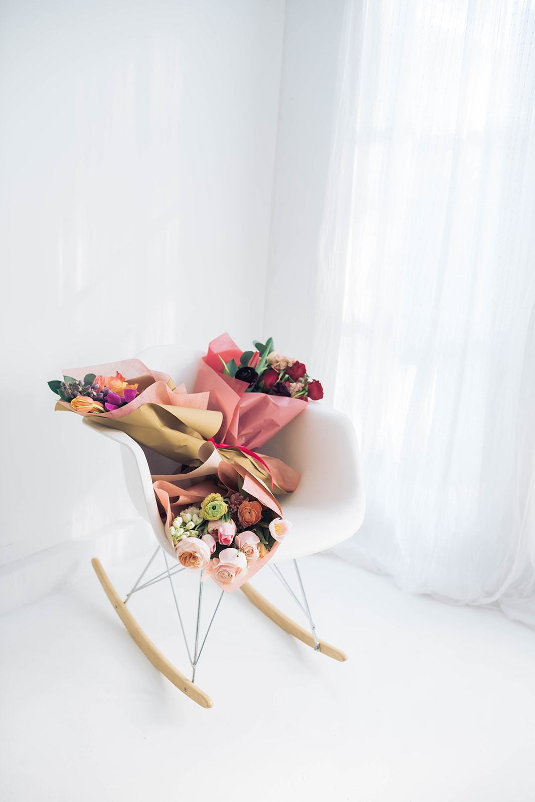 Two wrapped bouquets on a white chair by a bright window.