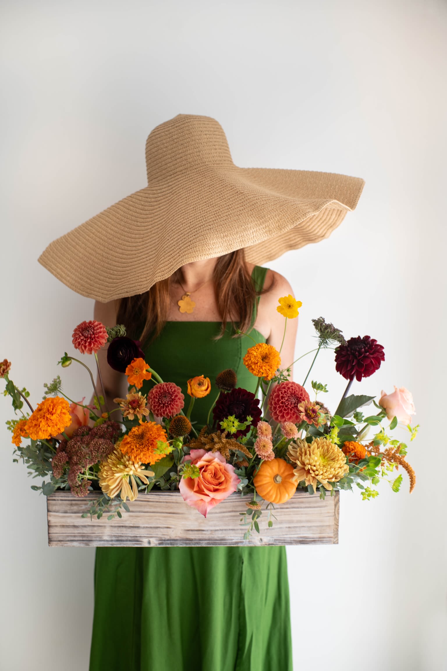 Woman in a green dress holding a wooden box of colorful flowers