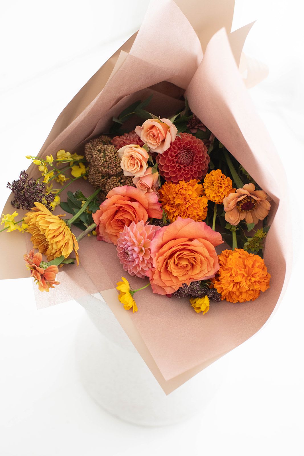 Bouquet of peach, orange, yellow, and pink flowers wrapped in blush paper
