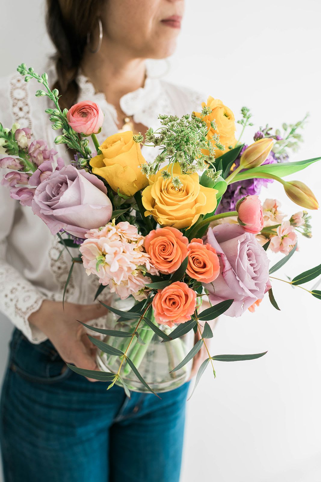 Woman holding a colorful bouquet of roses and tulips in a glass vase
