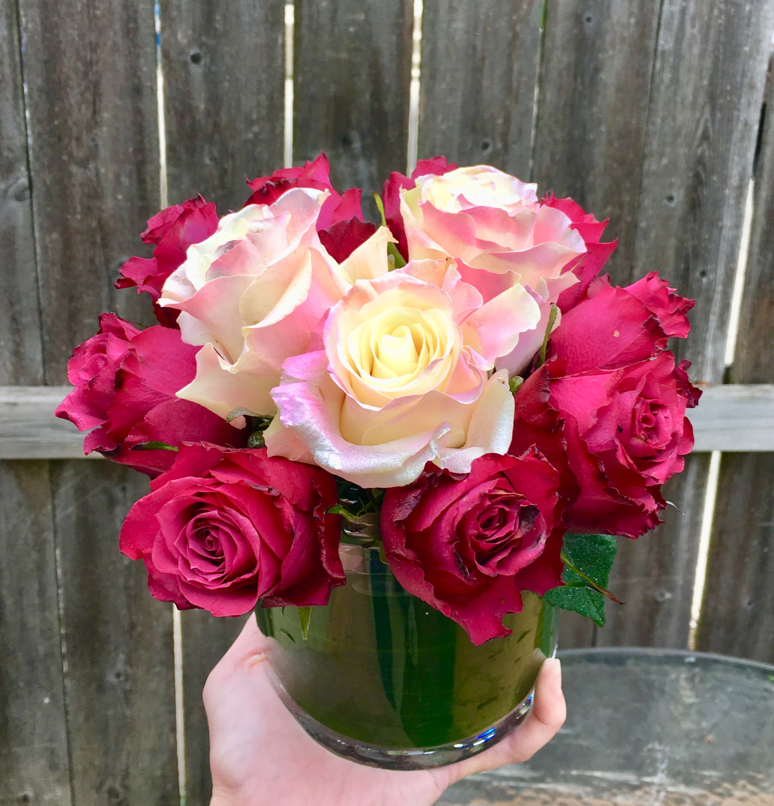 Short arrangement of cream and red roses in a clear glass vase held in one hand