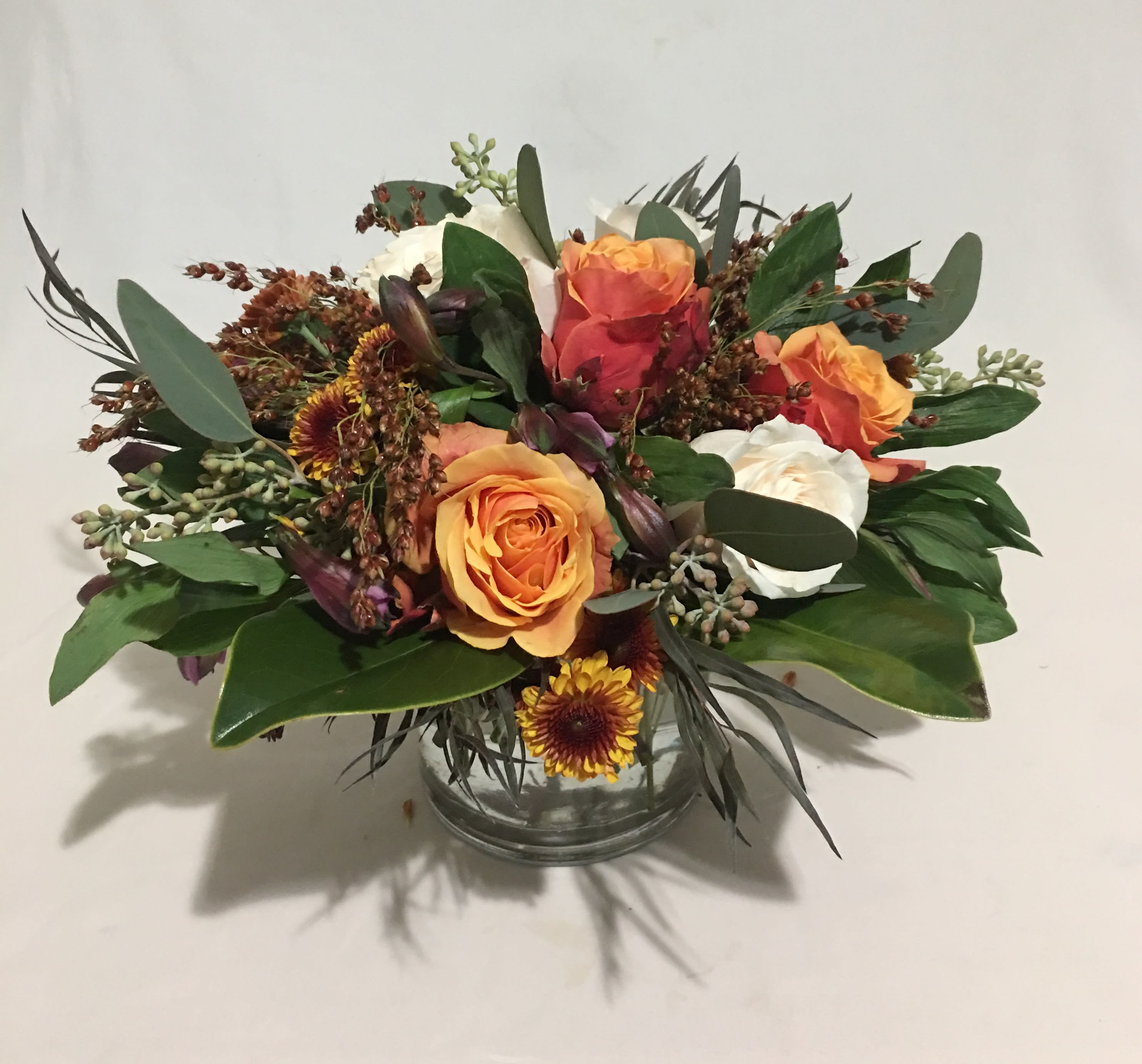 Low arrangement of orange and white roses with yellow mums in a clear glass vase