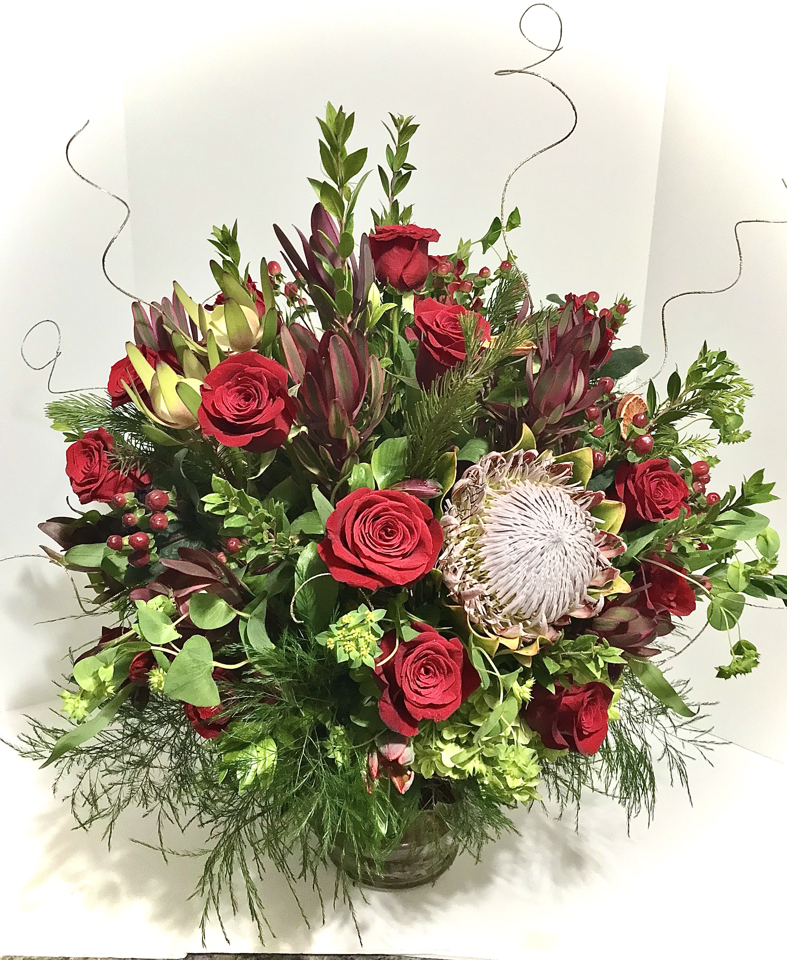 Large arrangement of red roses and king protea in a clear glass vase