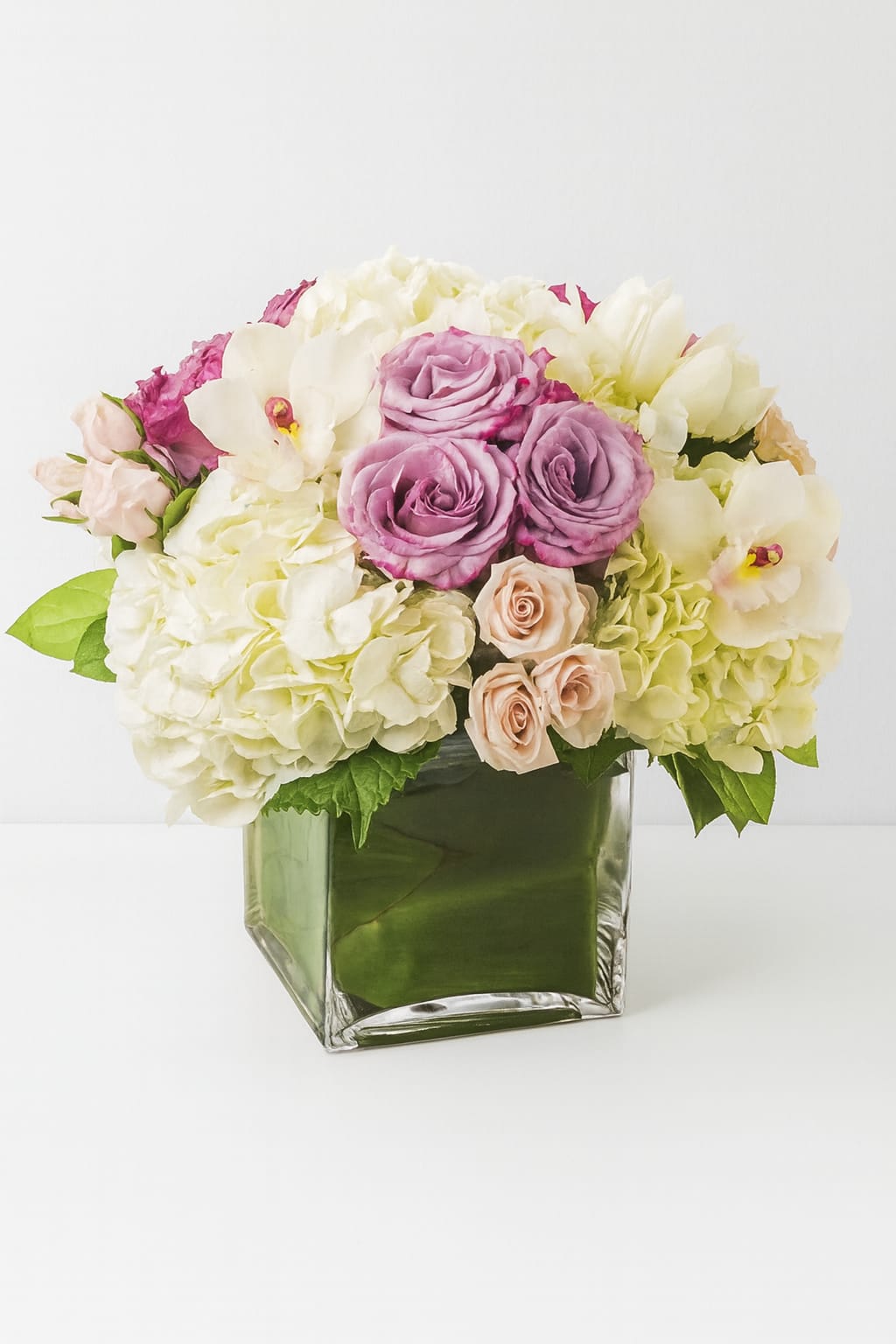 Mixed pink, white, and lavender flowers arranged in a square glass vase