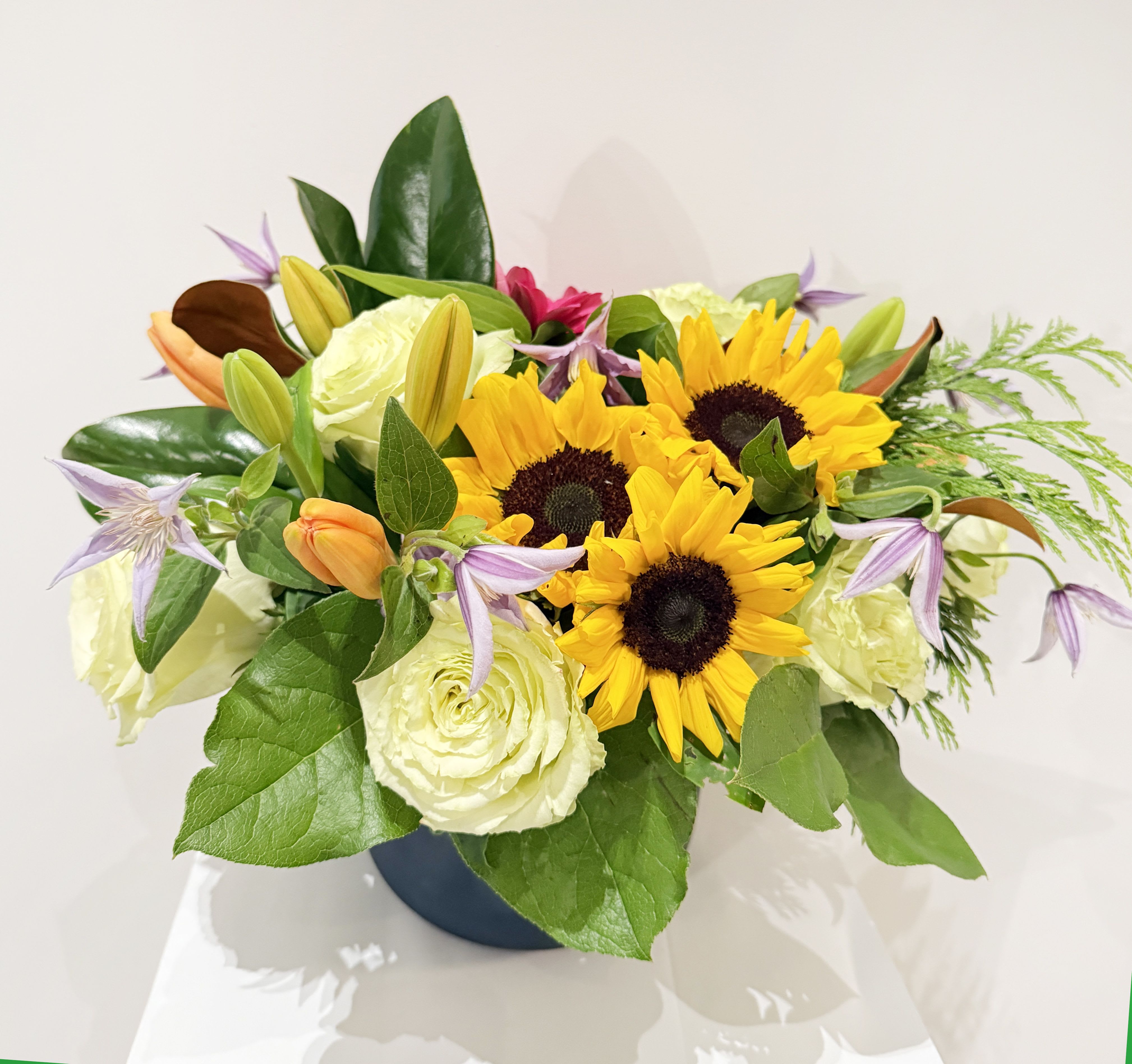 Bouquet of sunflowers, white roses, and lilies in a dark vase