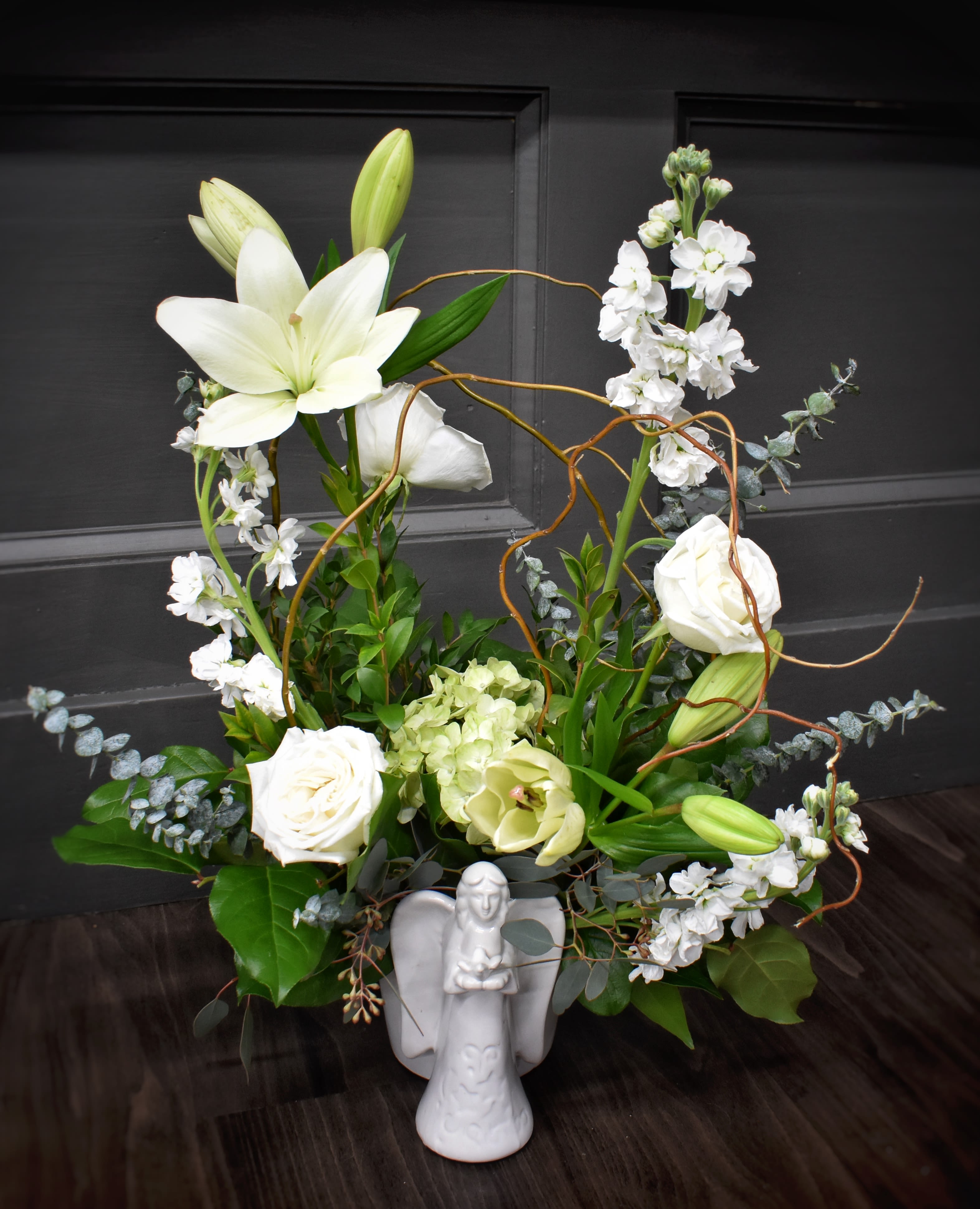 White lilies and roses arranged with greenery in a white angel vase